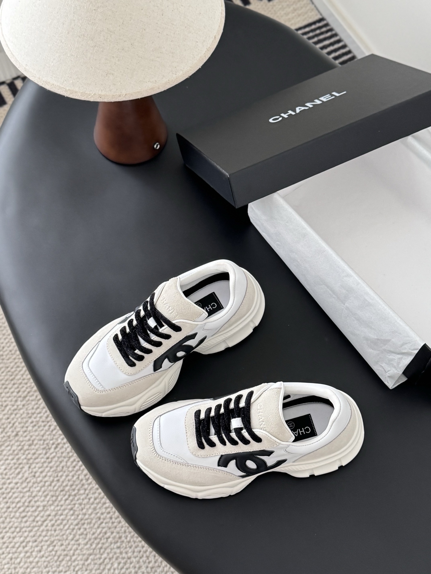 A pair of Chanel ivory and black suede leather sneakers with black CC logo and original black box on a table. - Hình 5
