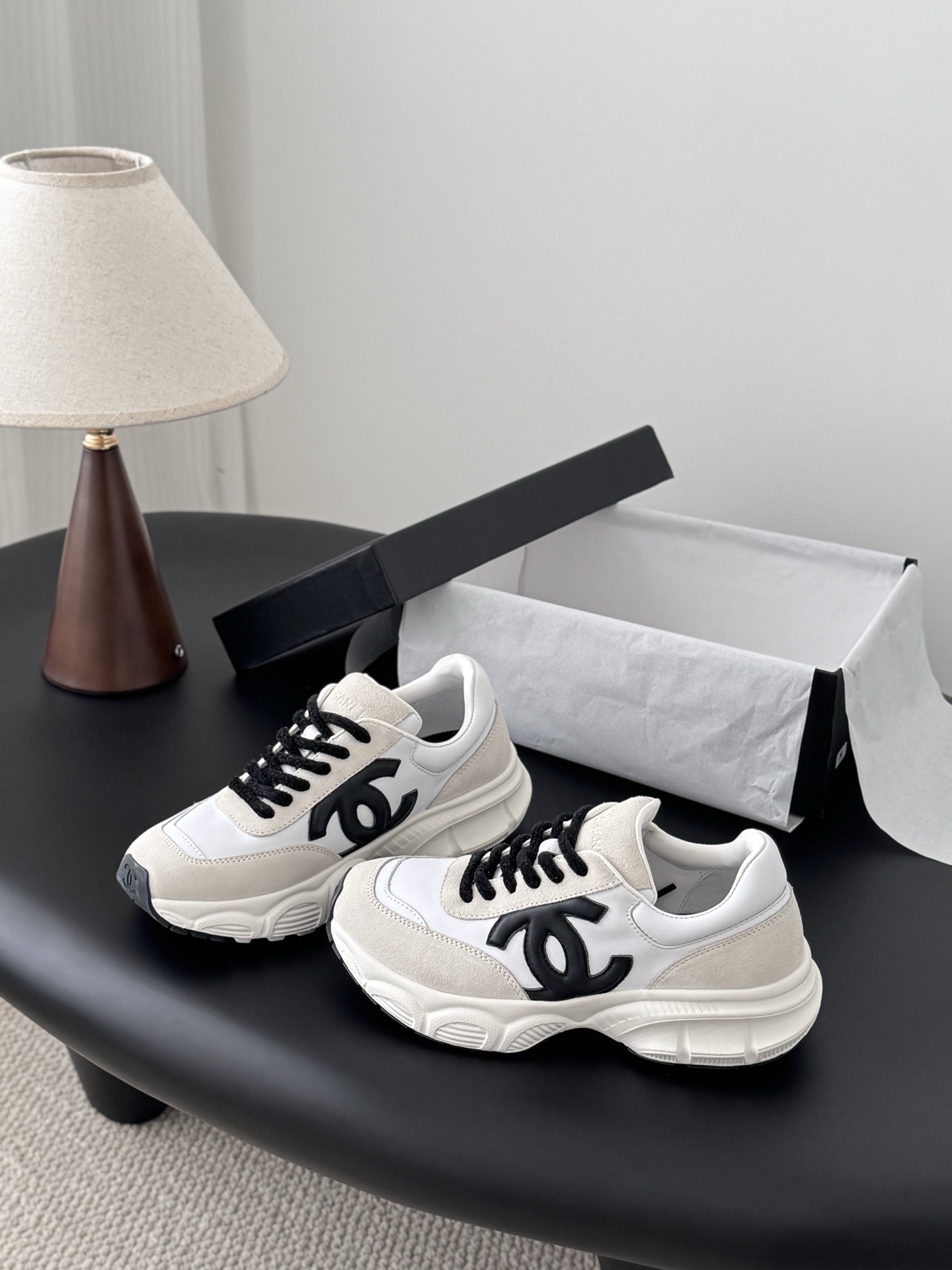 A pair of Chanel ivory and black suede leather sneakers with black CC logo and original black box on a table. - Hình 2