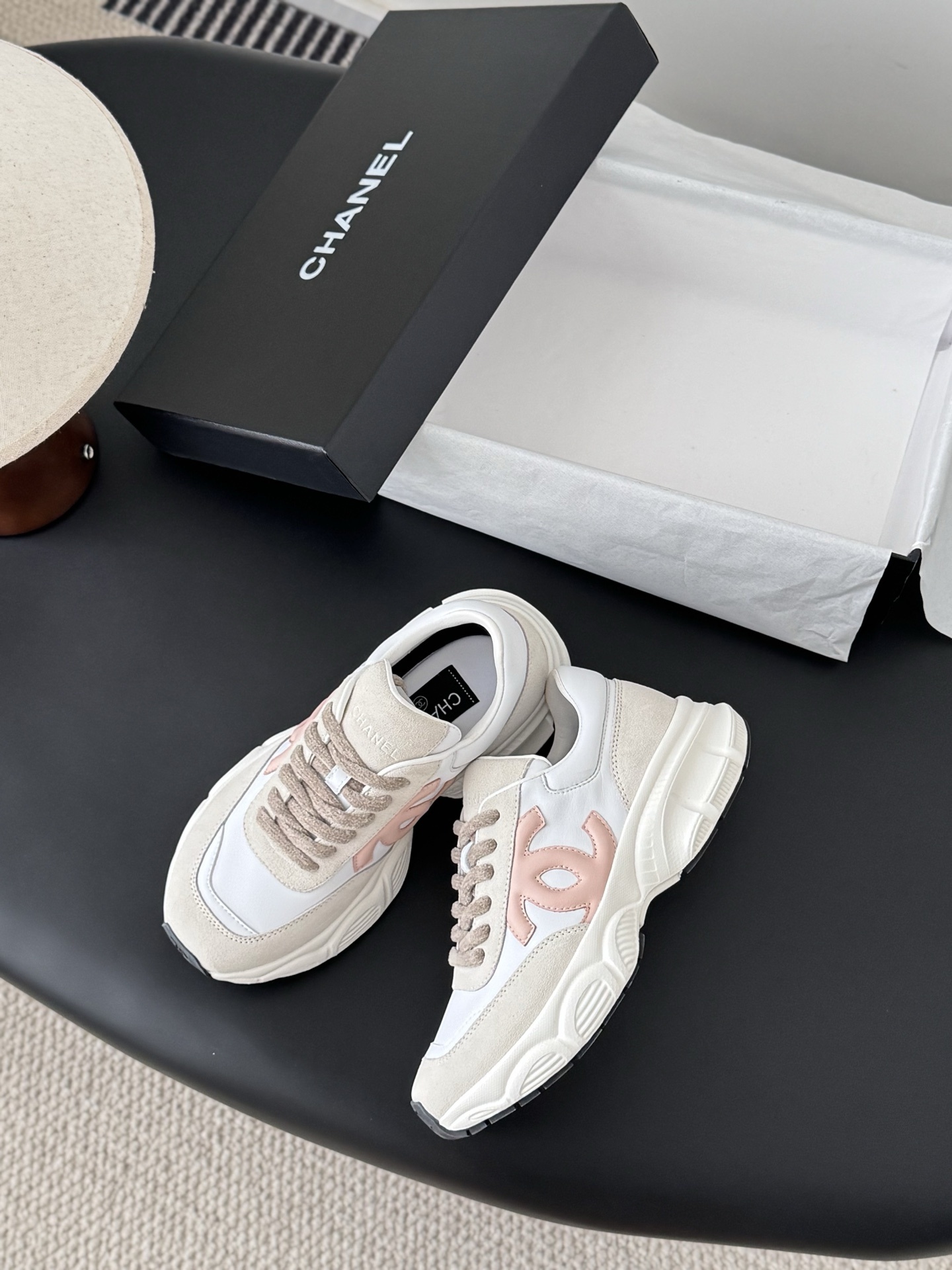 A pair of Chanel white and pink leather sneakers with chunky soles next to a black Chanel shoebox - Hình 3