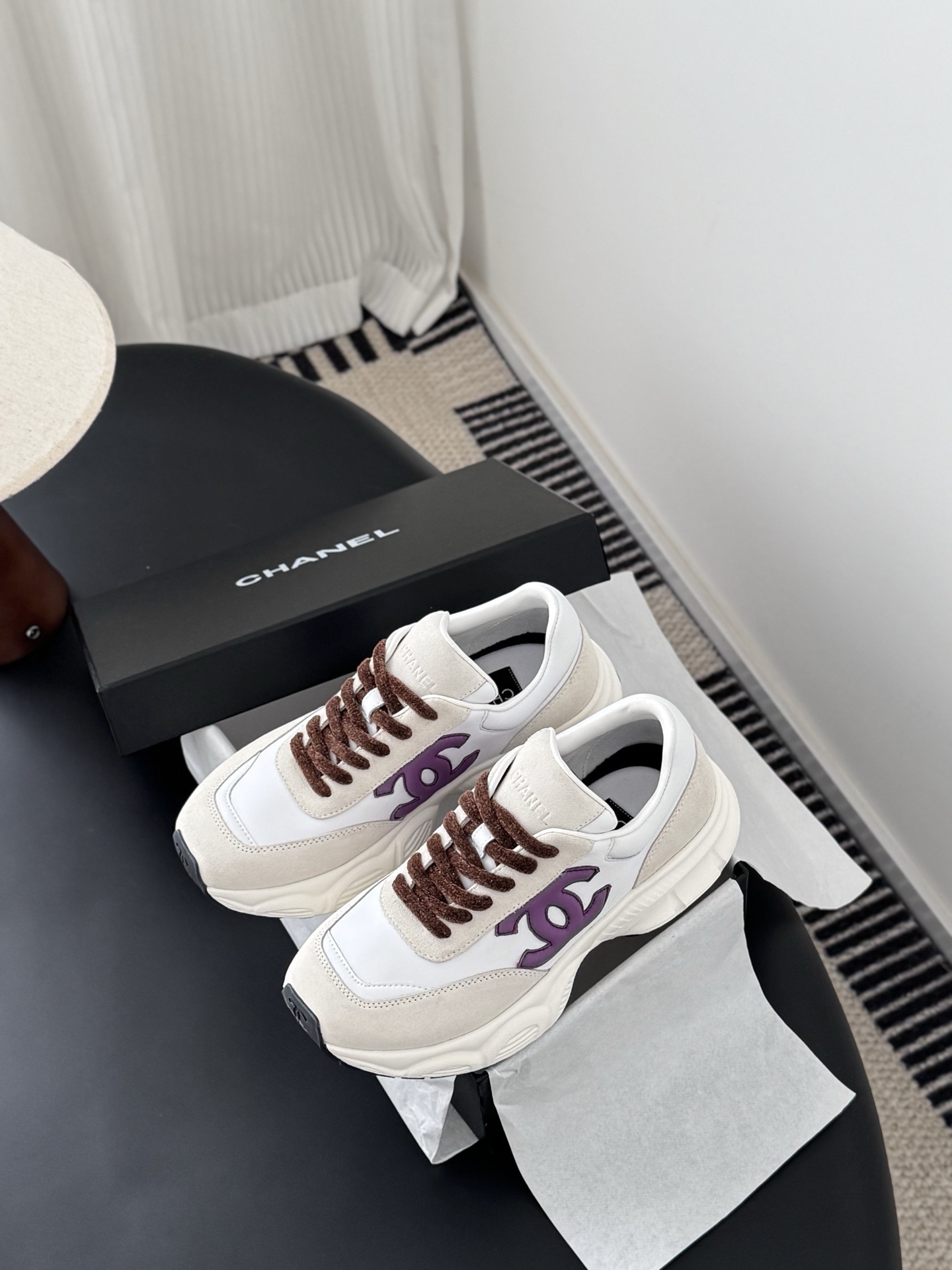 A pair of white and cream Chanel sneakers with purple CC logos and brown laces next to their original box. - Hình 9