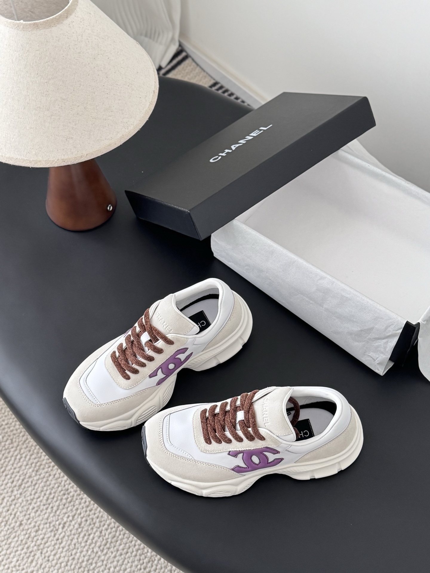 A pair of white and cream Chanel sneakers with purple CC logos and brown laces next to their original box. - Hình 8