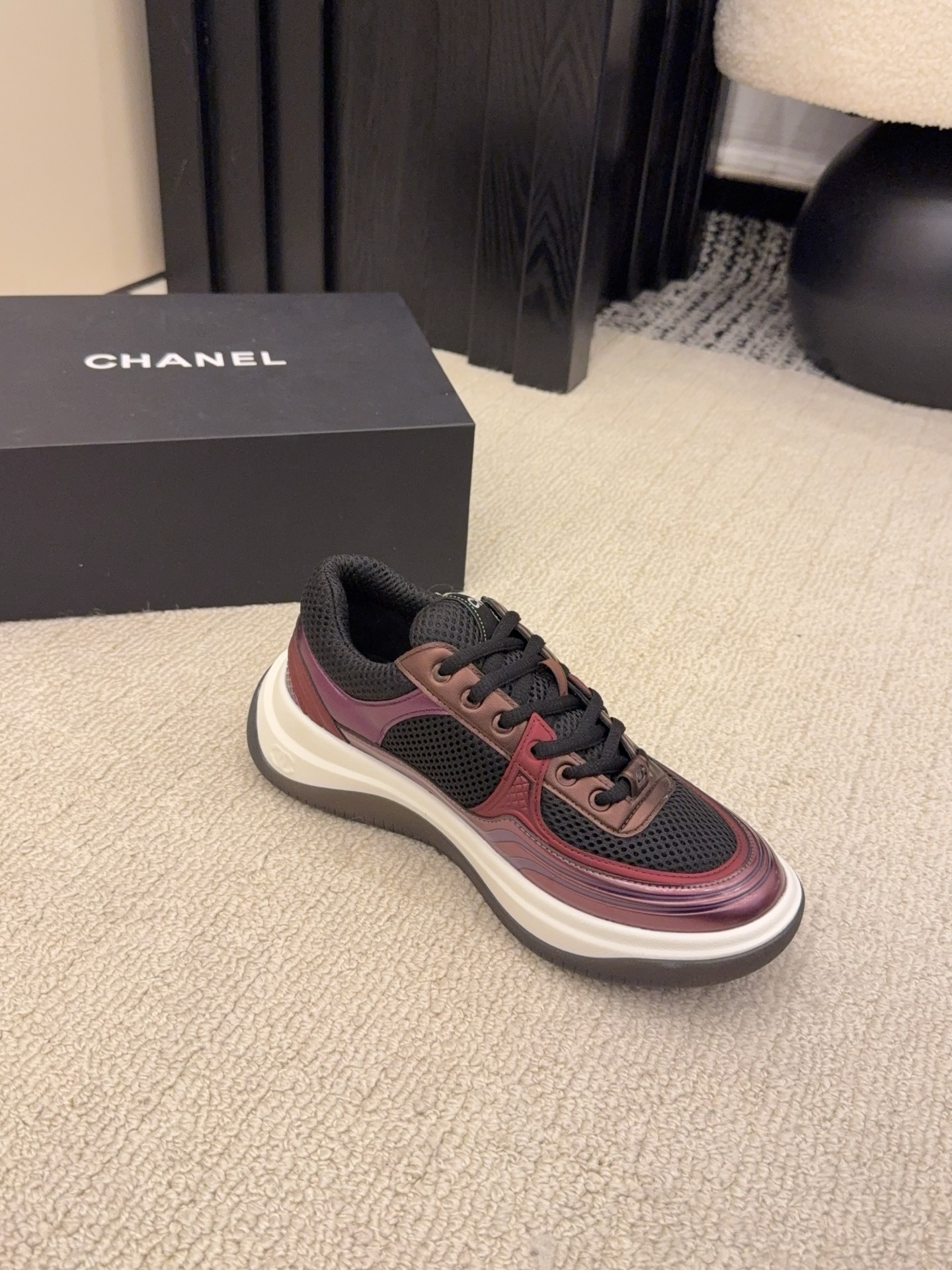 Two pairs of Chanel luxury sneakers in metallic olive and burgundy colorways displayed on a black box and carpet. - Hình 4