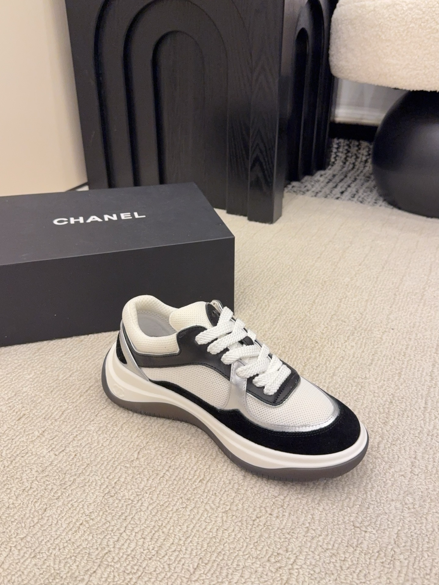 Top view of a pair of Chanel black and white sneakers with the iconic CC logo next to a black Chanel box - Hình 9