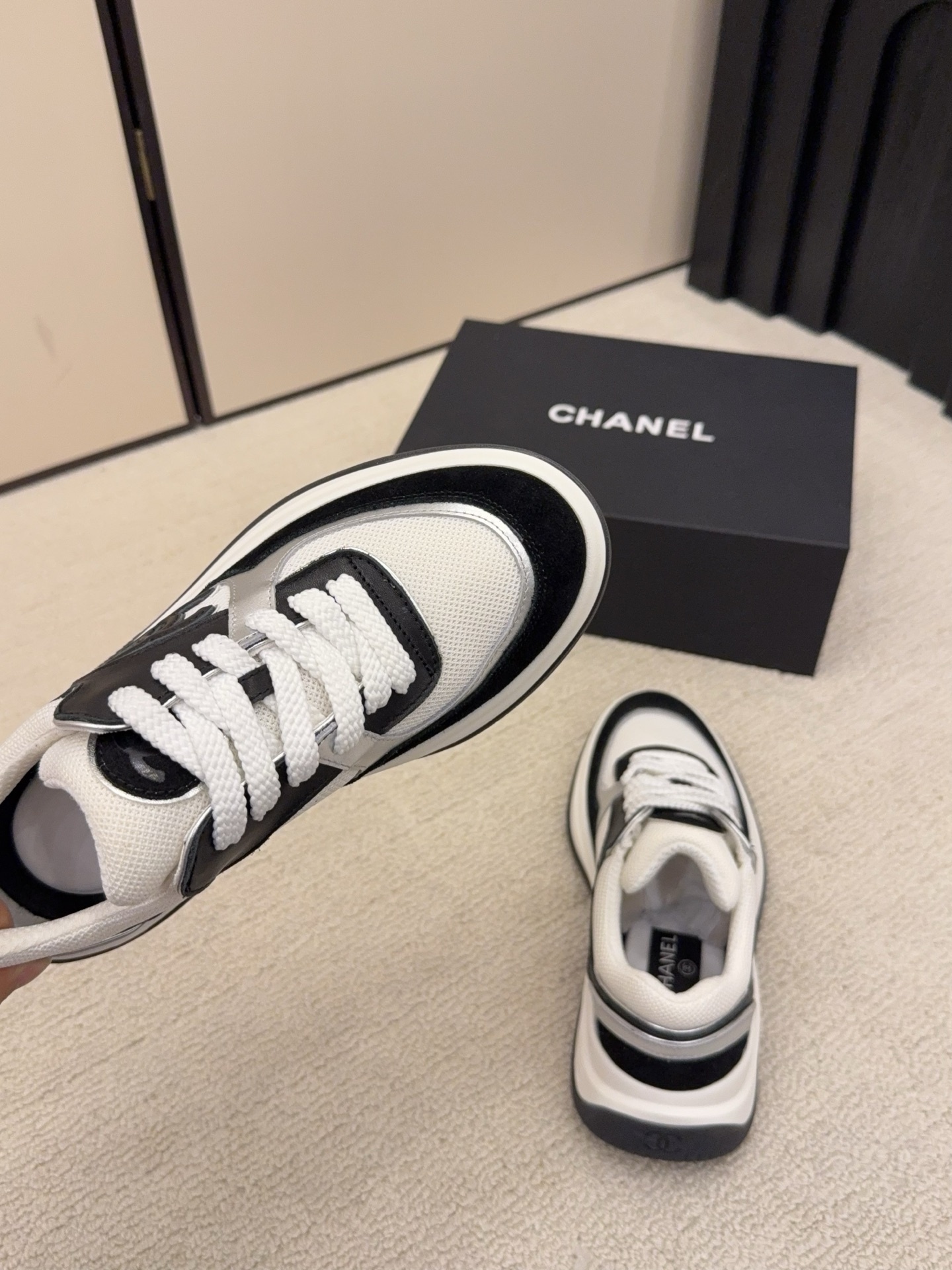 Top view of a pair of Chanel black and white sneakers with the iconic CC logo next to a black Chanel box - Hình 8