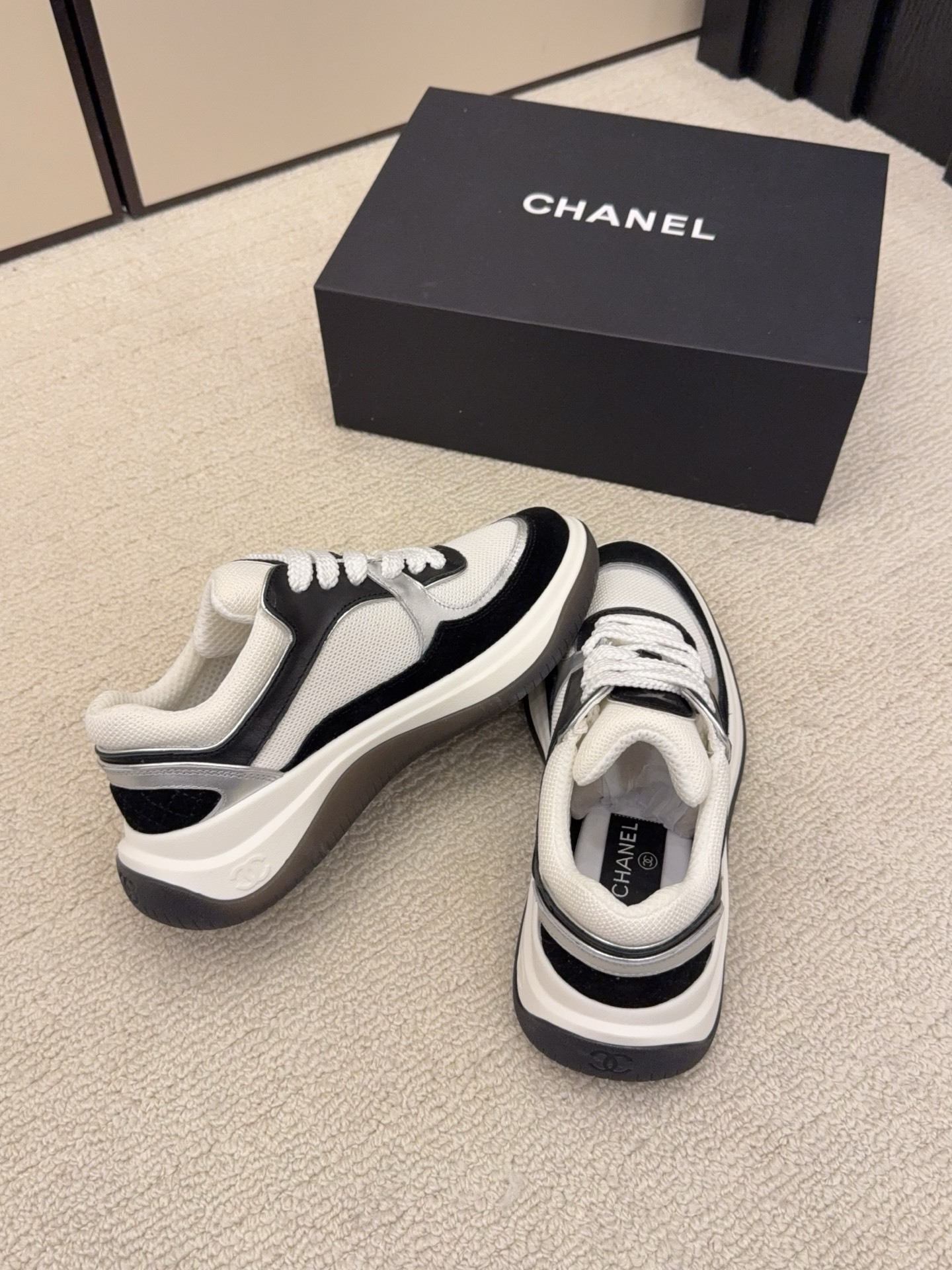 Top view of a pair of Chanel black and white sneakers with the iconic CC logo next to a black Chanel box - Hình 7