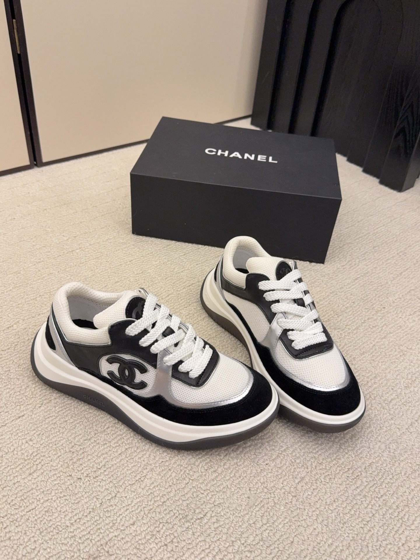 Top view of a pair of Chanel black and white sneakers with the iconic CC logo next to a black Chanel box - Hình 4