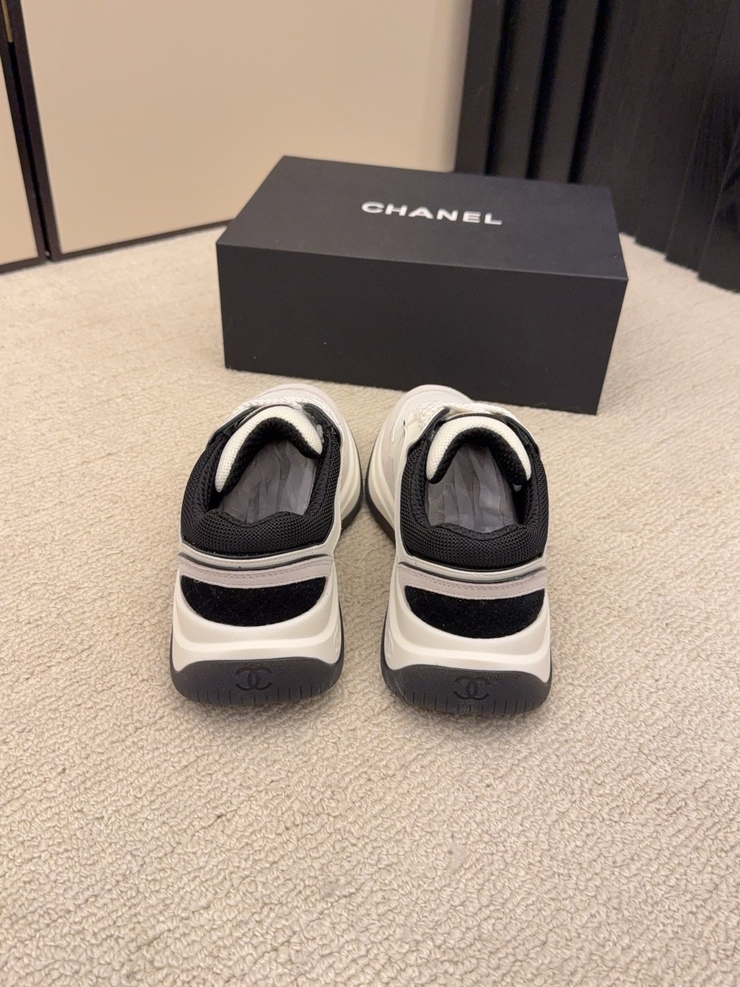 Pair of Chanel low-top sneakers in beige and black with the interlocking CC logo on the side next to a black shoe box. - Hình 8