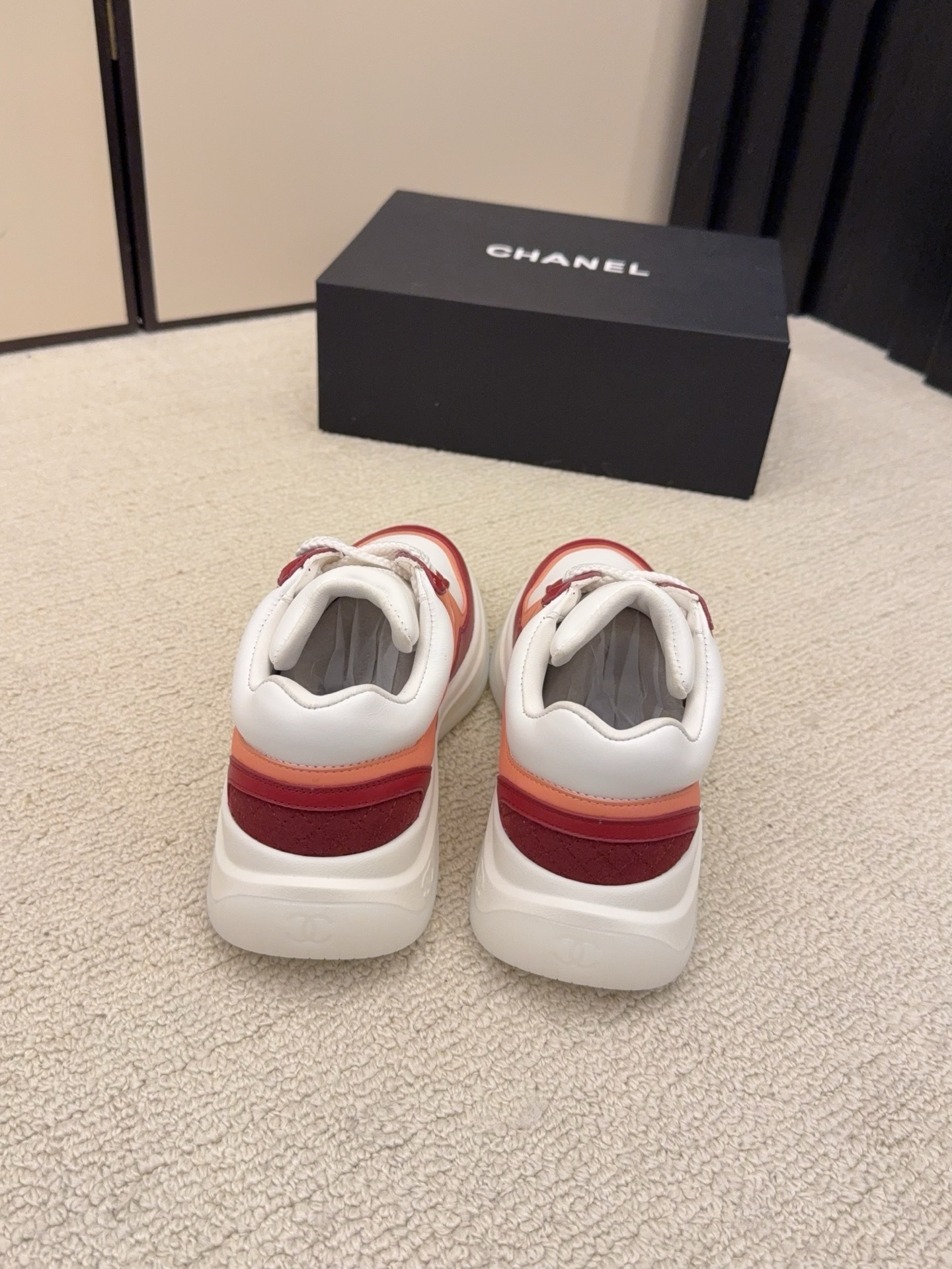 A pair of Chanel women's low-top sneakers in red, white, and orange leather with thick white laces next to a black Chanel box. - Hình 6