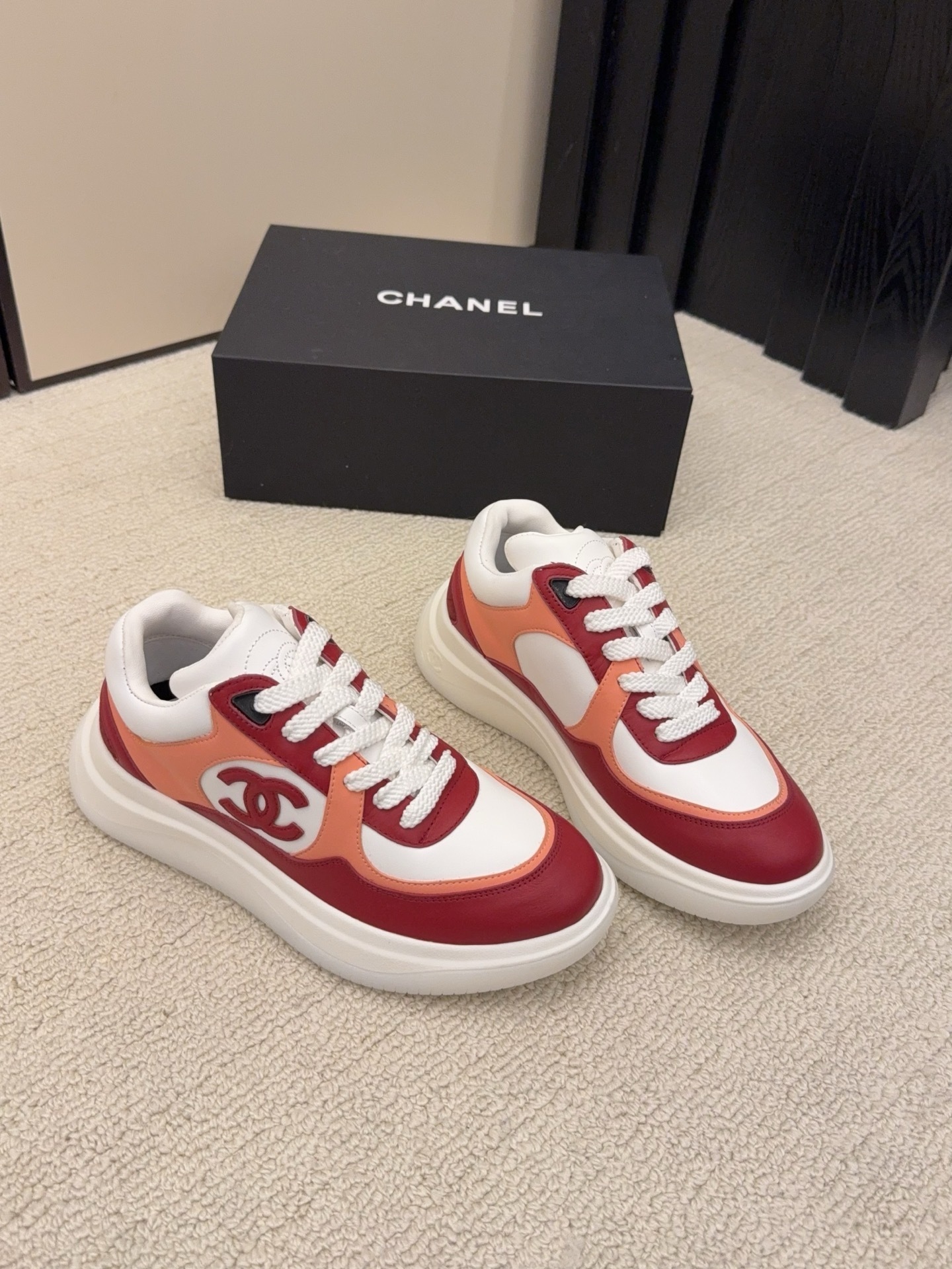 A pair of Chanel women's low-top sneakers in red, white, and orange leather with thick white laces next to a black Chanel box. - Hình 4
