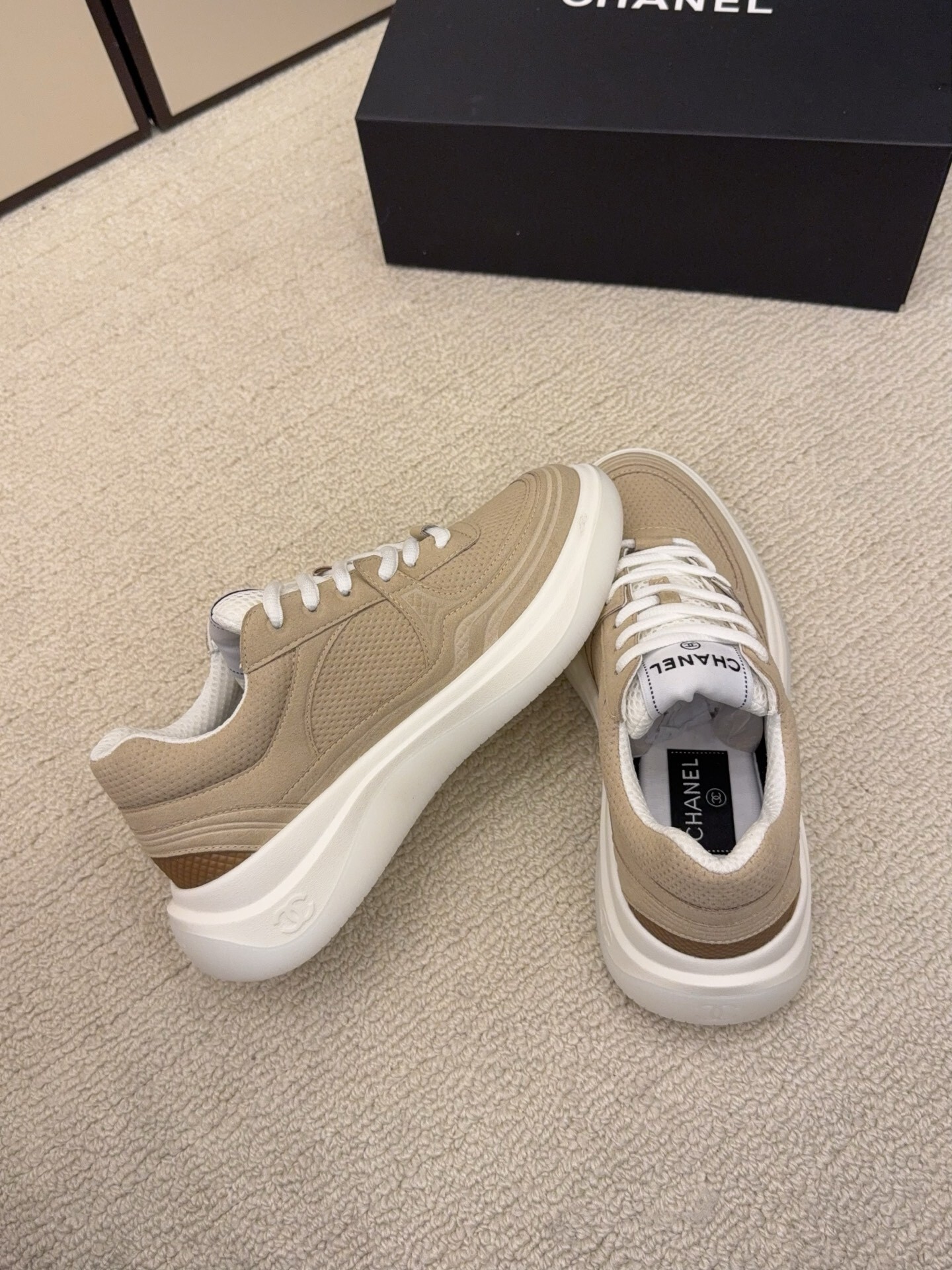 A pair of black and a pair of beige Chanel luxury platform sneakers with mesh detailing and interlocking CC logo displayed on a carpeted floor. - Hình 9