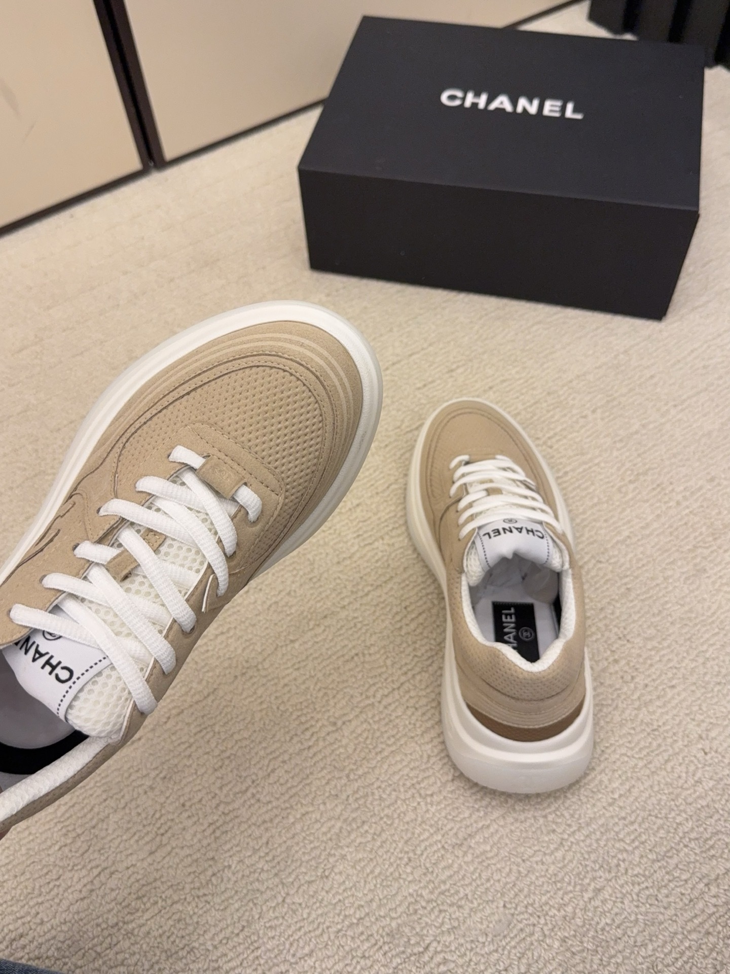 A pair of black and a pair of beige Chanel luxury platform sneakers with mesh detailing and interlocking CC logo displayed on a carpeted floor. - Hình 8