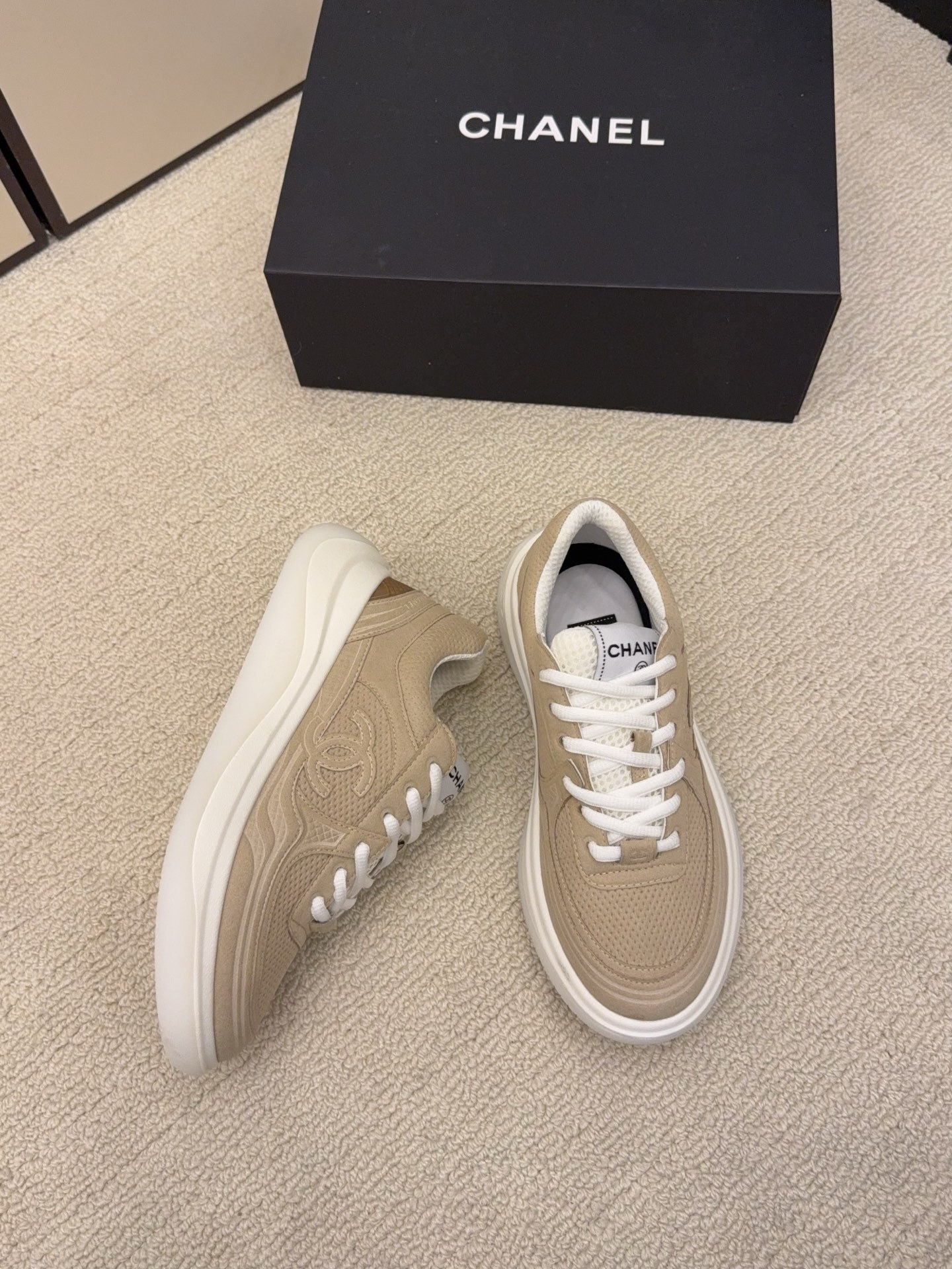 A pair of black and a pair of beige Chanel luxury platform sneakers with mesh detailing and interlocking CC logo displayed on a carpeted floor. - Hình 7