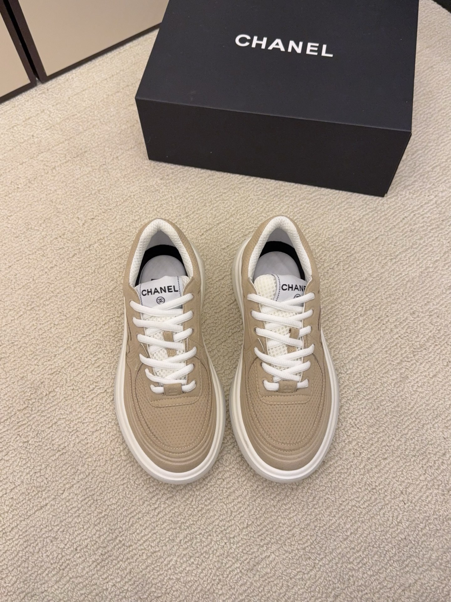 A pair of black and a pair of beige Chanel luxury platform sneakers with mesh detailing and interlocking CC logo displayed on a carpeted floor. - Hình 6