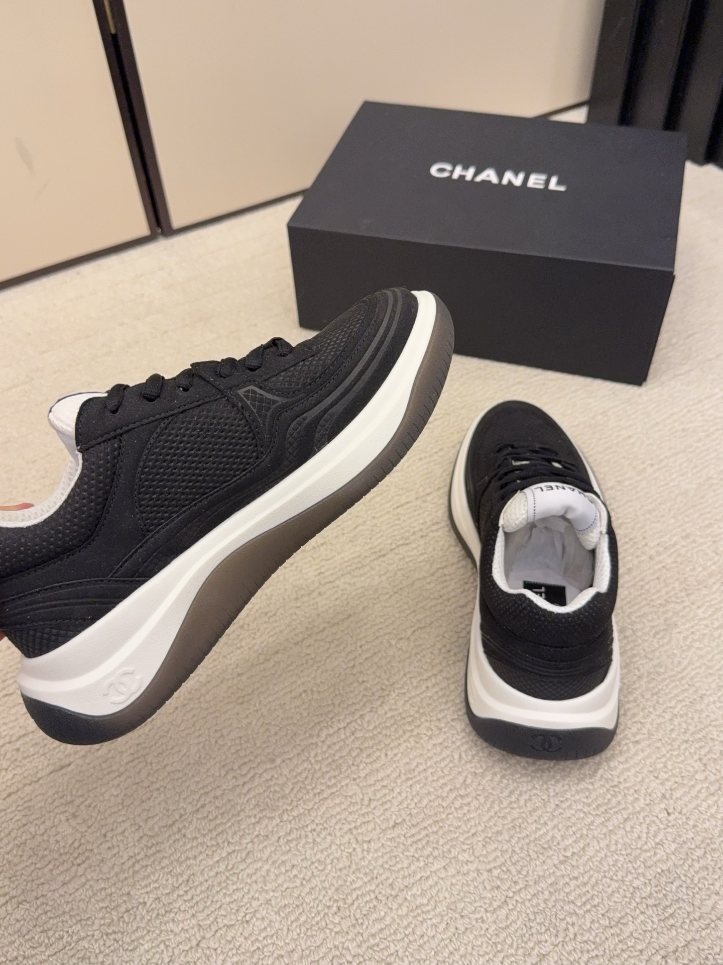 A pair of black and a pair of beige Chanel luxury platform sneakers with mesh detailing and interlocking CC logo displayed on a carpeted floor. - Hình 5