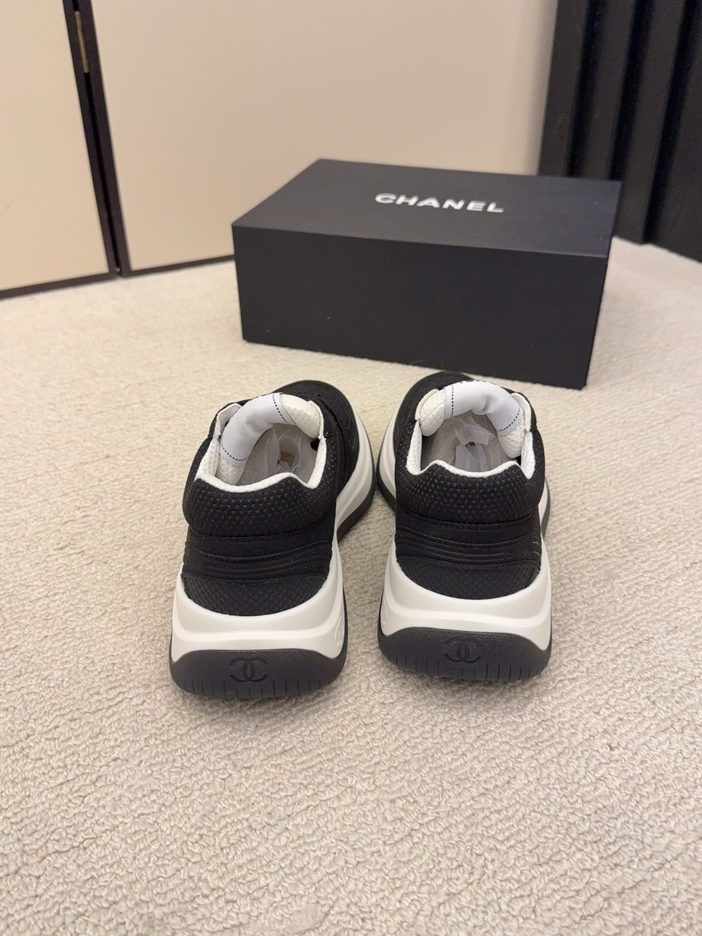 A pair of black and a pair of beige Chanel luxury platform sneakers with mesh detailing and interlocking CC logo displayed on a carpeted floor. - Hình 4