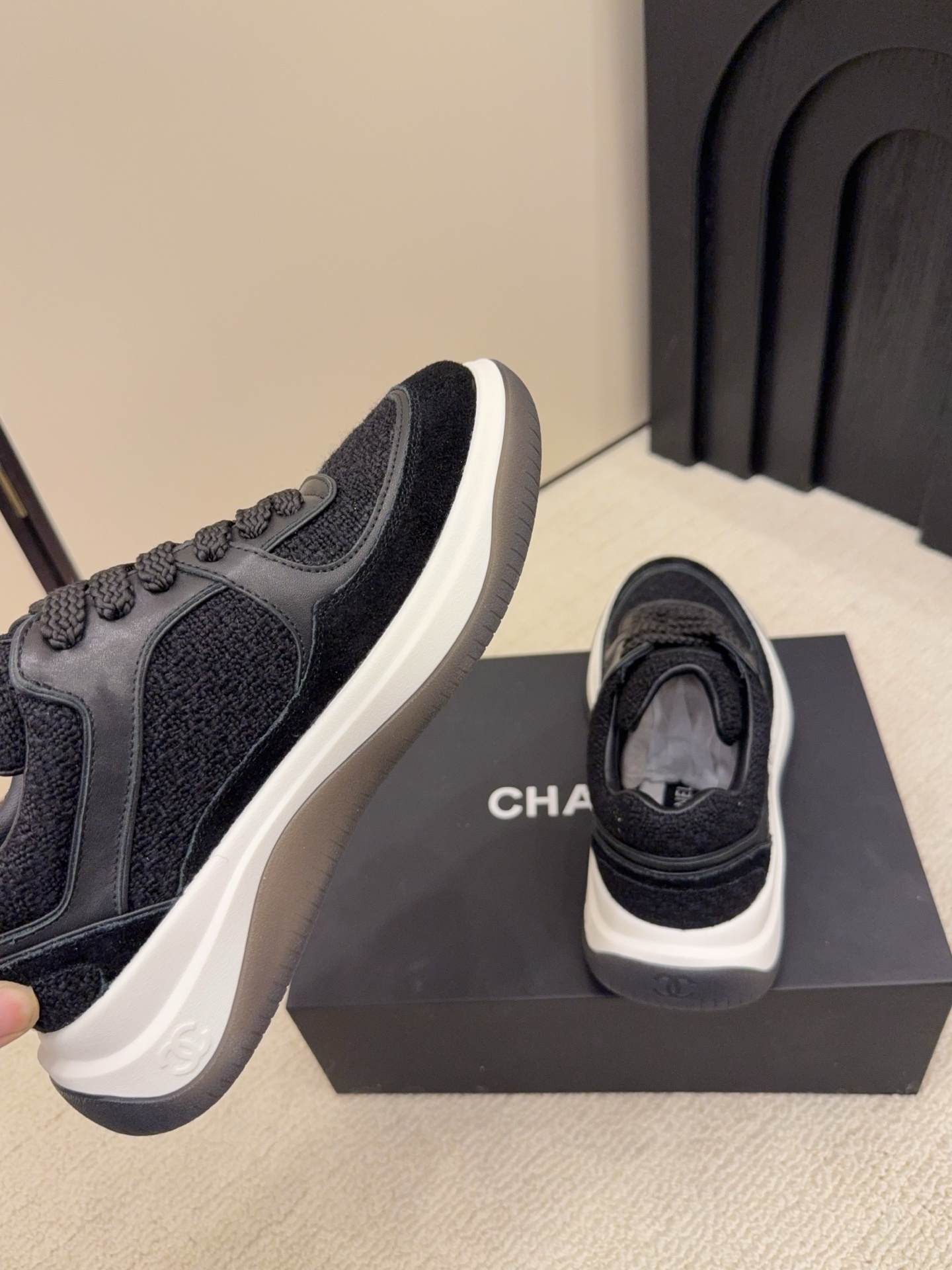 A pair of luxury black Chanel sneakers made of tweed and leather with white chunky soles on a black box. - Hình 9