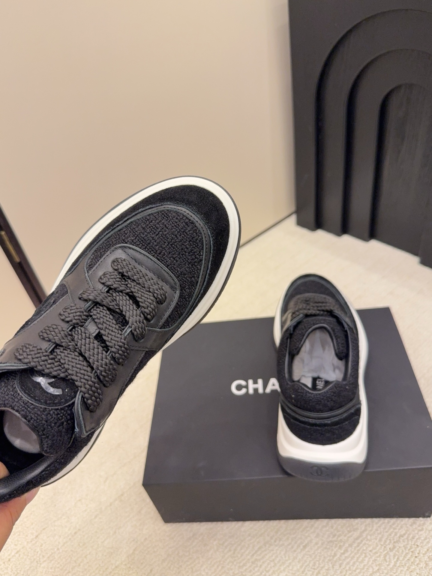 A pair of luxury black Chanel sneakers made of tweed and leather with white chunky soles on a black box. - Hình 8