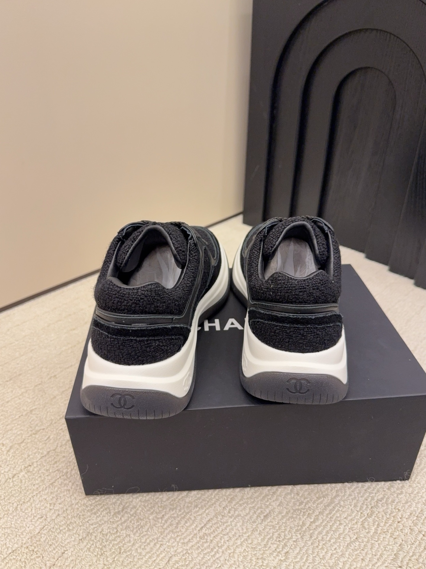 A pair of luxury black Chanel sneakers made of tweed and leather with white chunky soles on a black box. - Hình 7