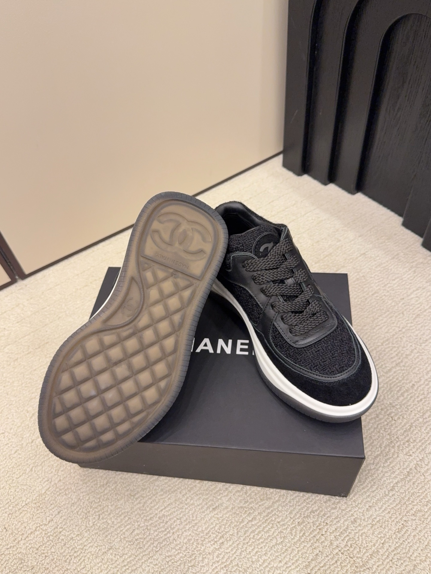 A pair of luxury black Chanel sneakers made of tweed and leather with white chunky soles on a black box. - Hình 6