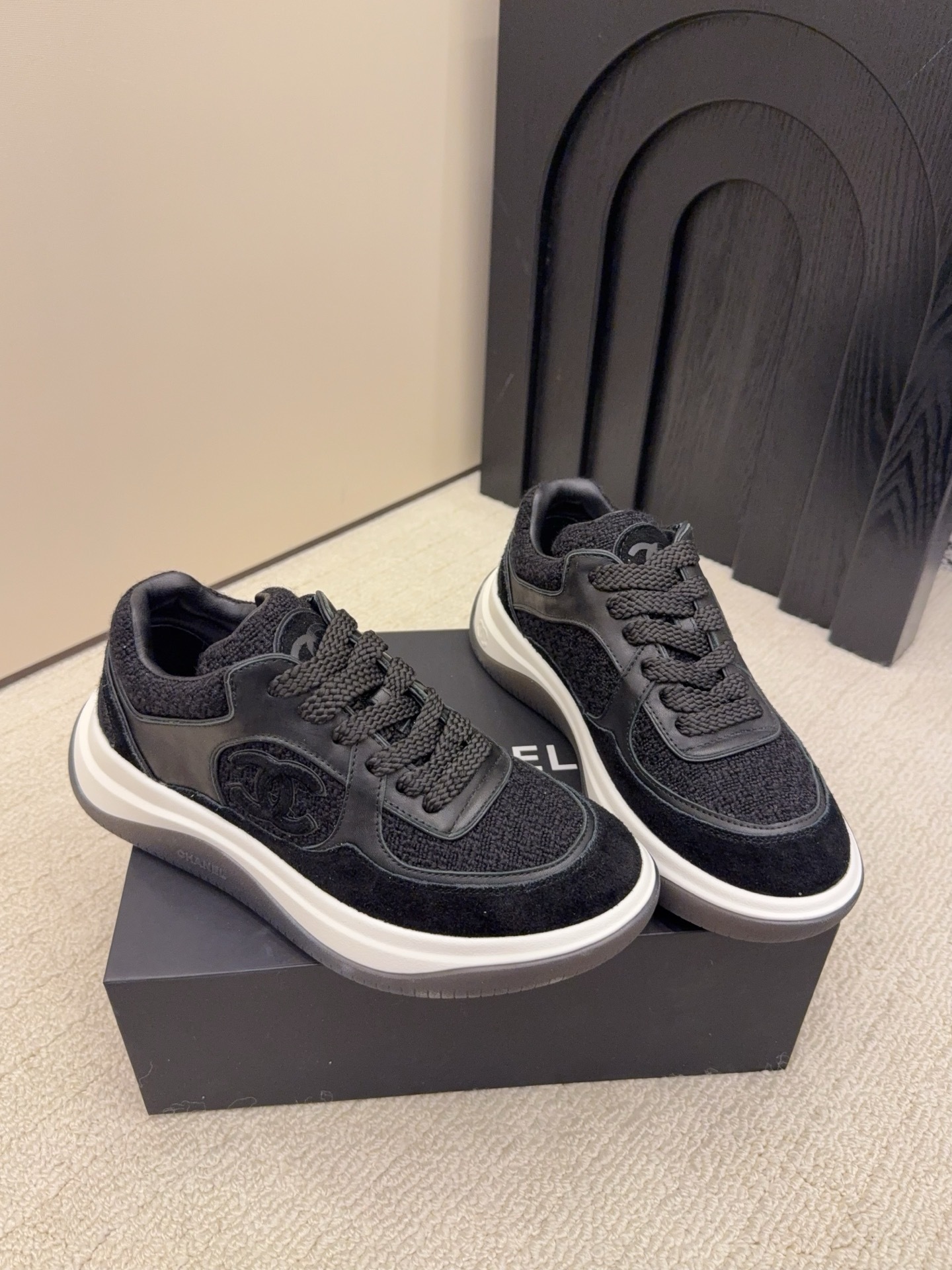 A pair of luxury black Chanel sneakers made of tweed and leather with white chunky soles on a black box. - Hình 5