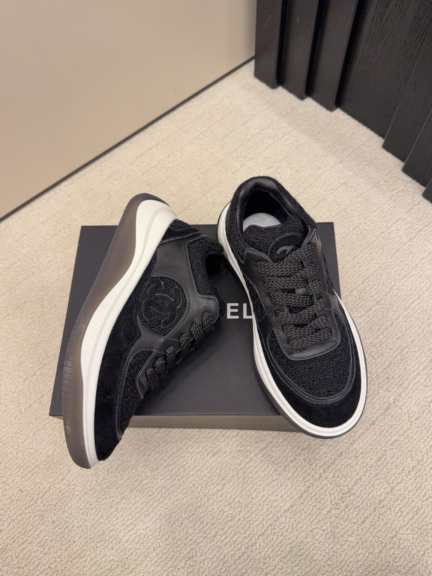 A pair of luxury black Chanel sneakers made of tweed and leather with white chunky soles on a black box. - Hình 4