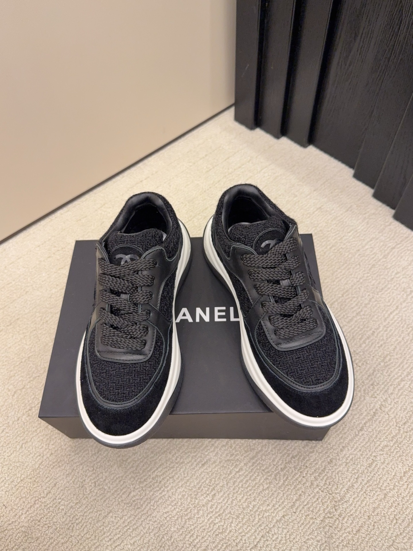 A pair of luxury black Chanel sneakers made of tweed and leather with white chunky soles on a black box. - Hình 3