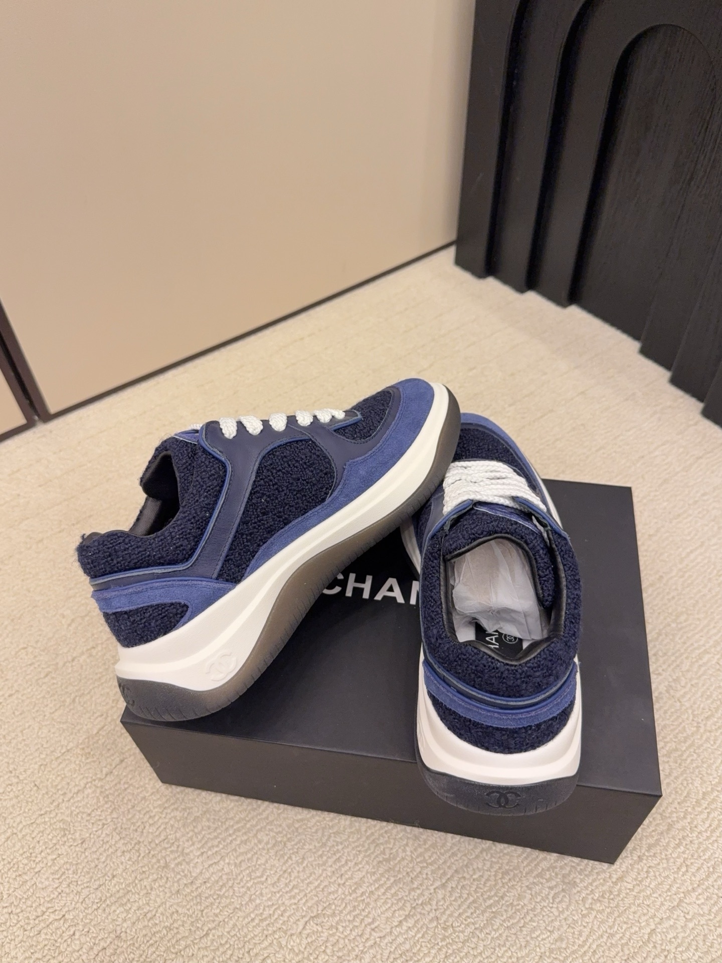 A pair of Chanel navy blue sneakers featuring tweed and suede panels with white laces on a Chanel shoe box. - Hình 9