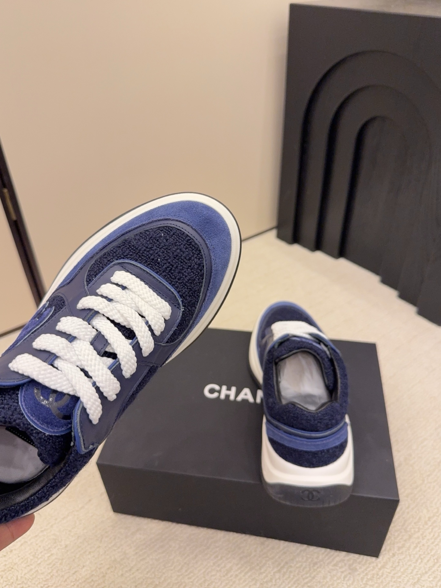 A pair of Chanel navy blue sneakers featuring tweed and suede panels with white laces on a Chanel shoe box. - Hình 8