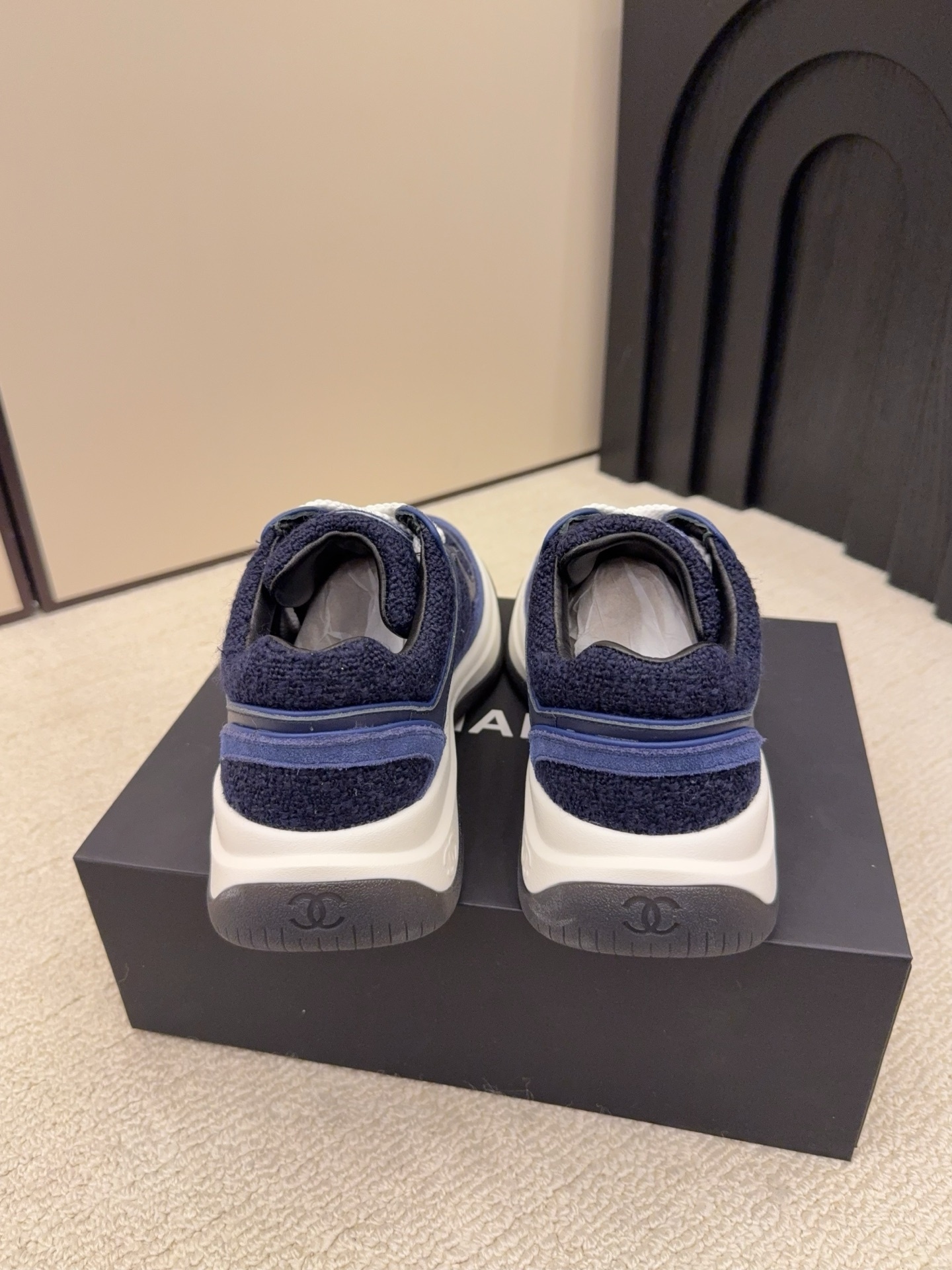 A pair of Chanel navy blue sneakers featuring tweed and suede panels with white laces on a Chanel shoe box. - Hình 7
