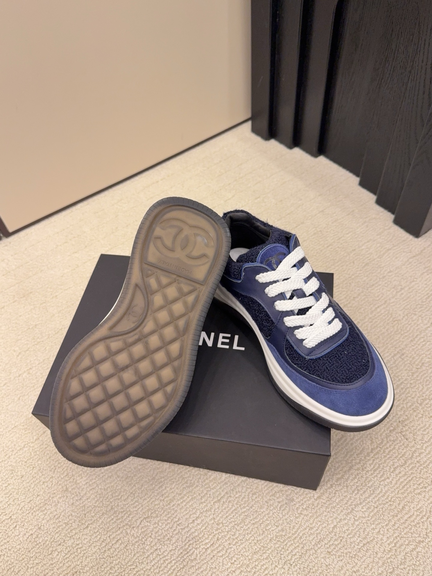 A pair of Chanel navy blue sneakers featuring tweed and suede panels with white laces on a Chanel shoe box. - Hình 6