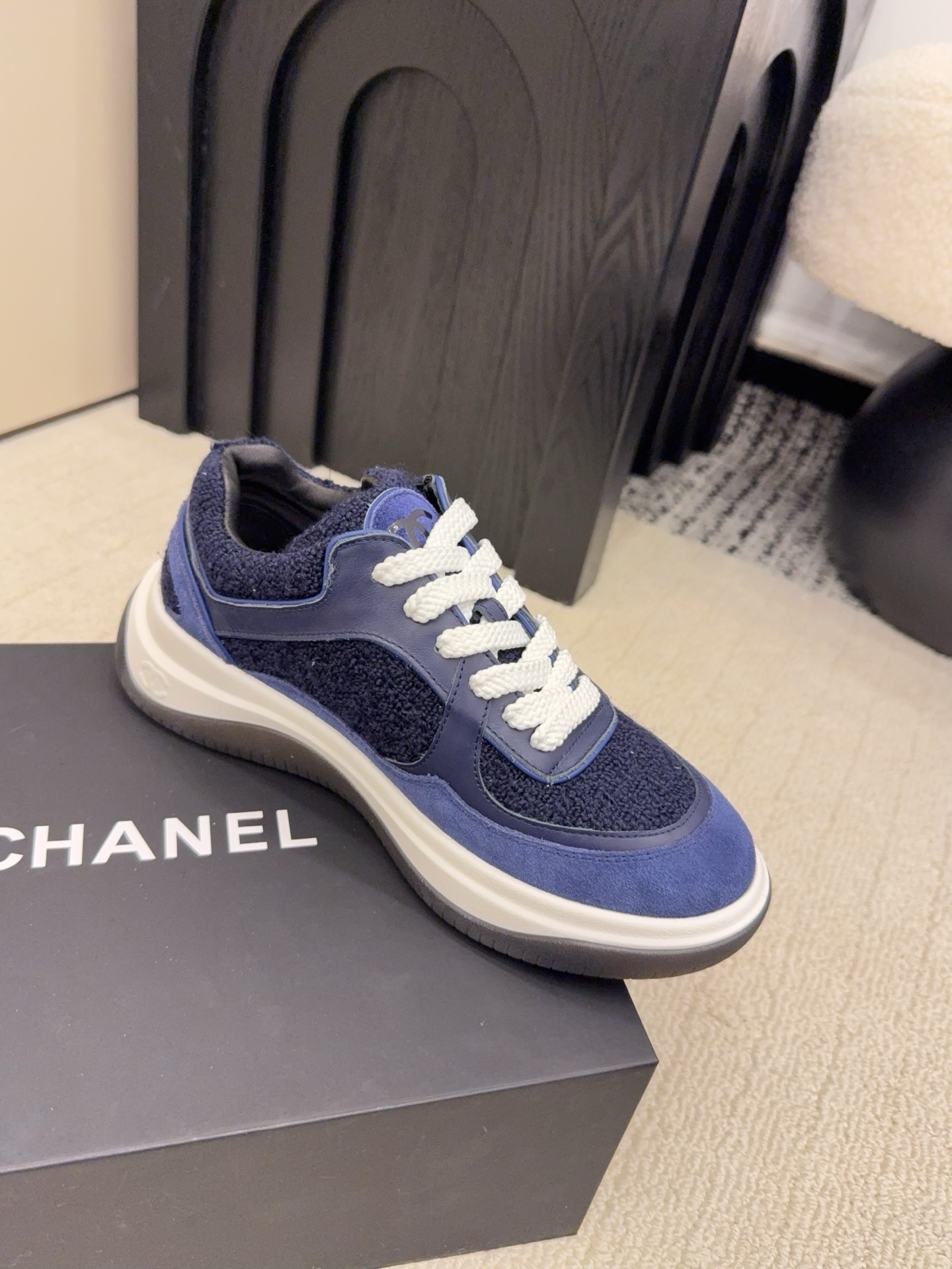 A pair of Chanel navy blue sneakers featuring tweed and suede panels with white laces on a Chanel shoe box. - Hình 5