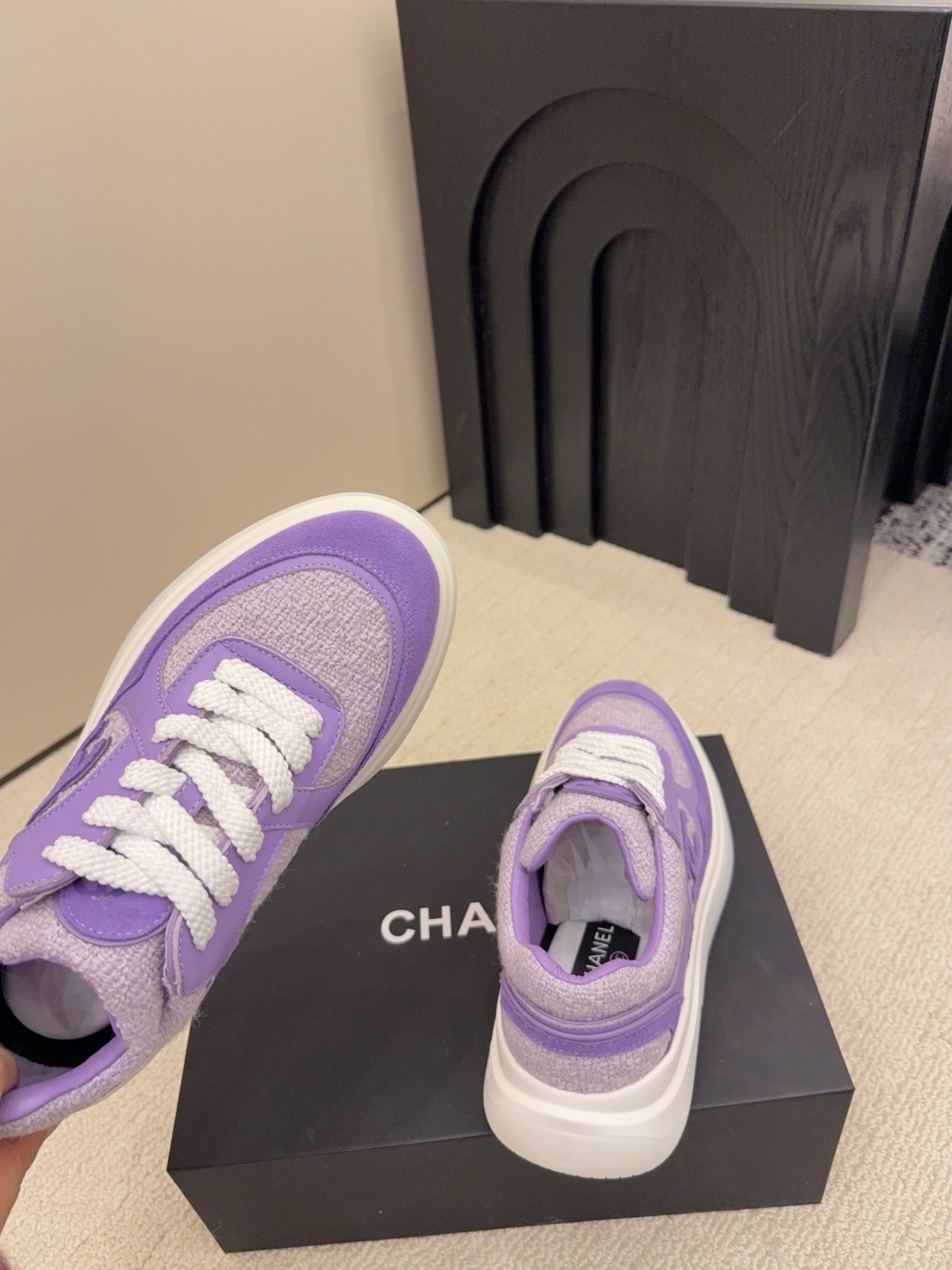 A pair of luxury Chanel purple tweed and suede sneakers with white chunky soles and white laces placed on a black designer shoe box. - Hình 9