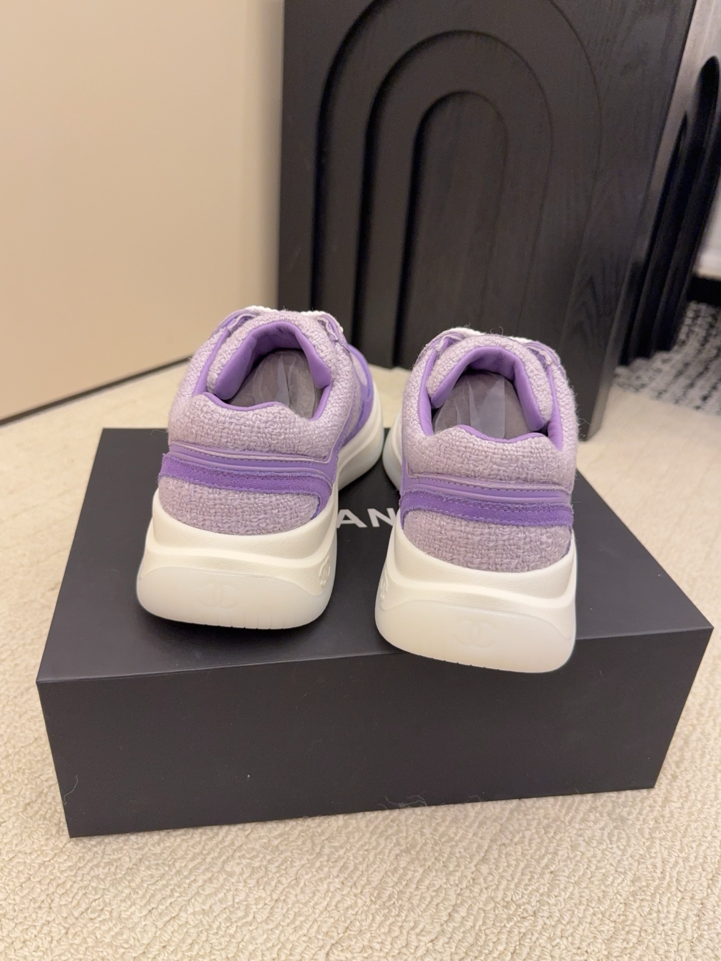 A pair of luxury Chanel purple tweed and suede sneakers with white chunky soles and white laces placed on a black designer shoe box. - Hình 8