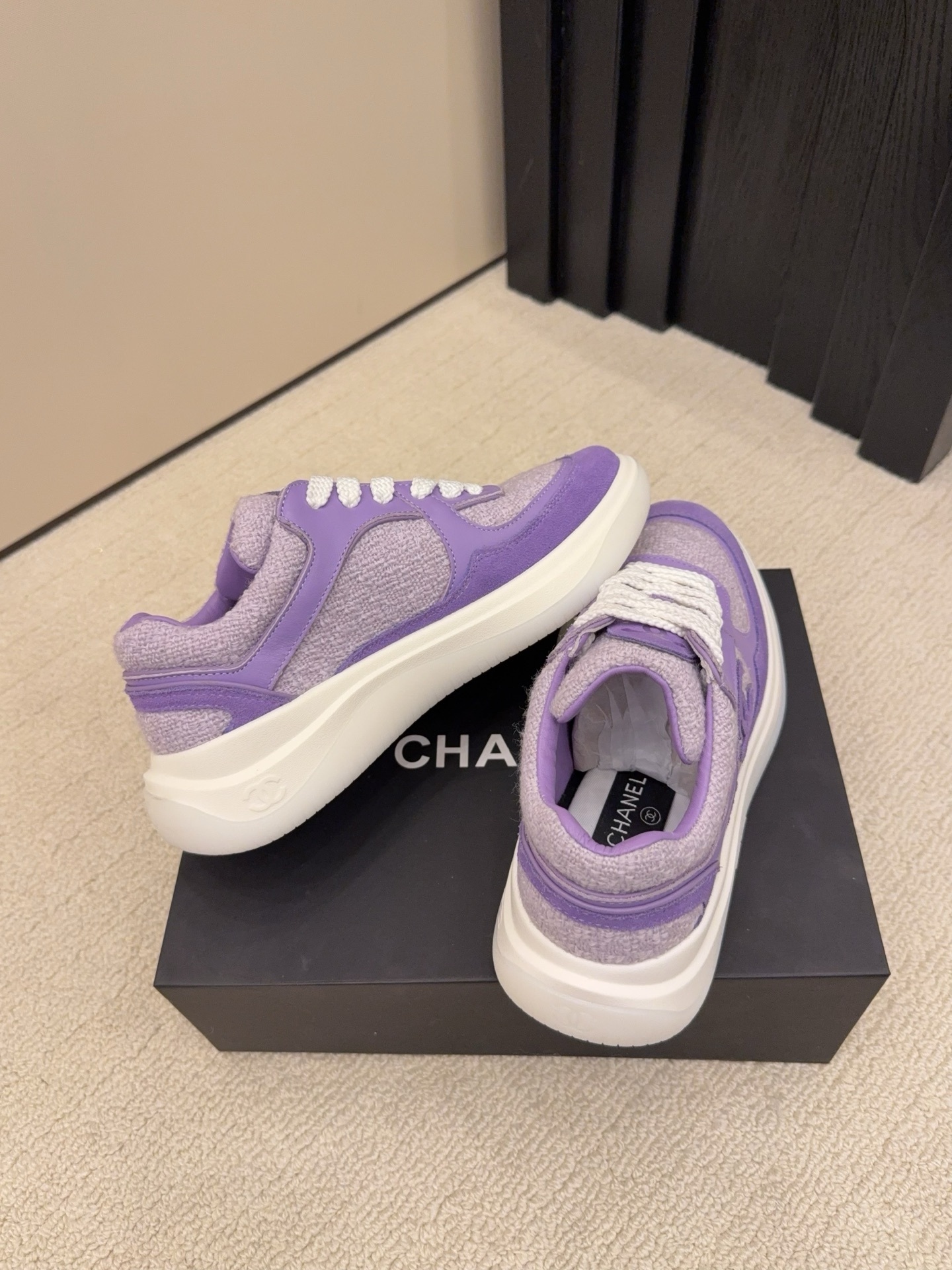 A pair of luxury Chanel purple tweed and suede sneakers with white chunky soles and white laces placed on a black designer shoe box. - Hình 7
