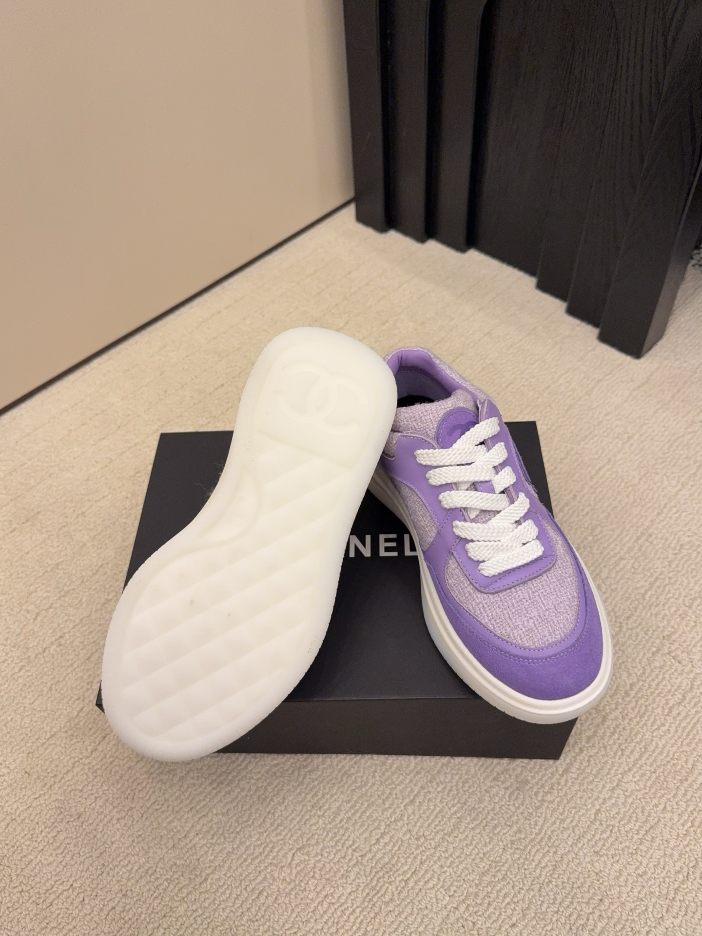 A pair of luxury Chanel purple tweed and suede sneakers with white chunky soles and white laces placed on a black designer shoe box. - Hình 6