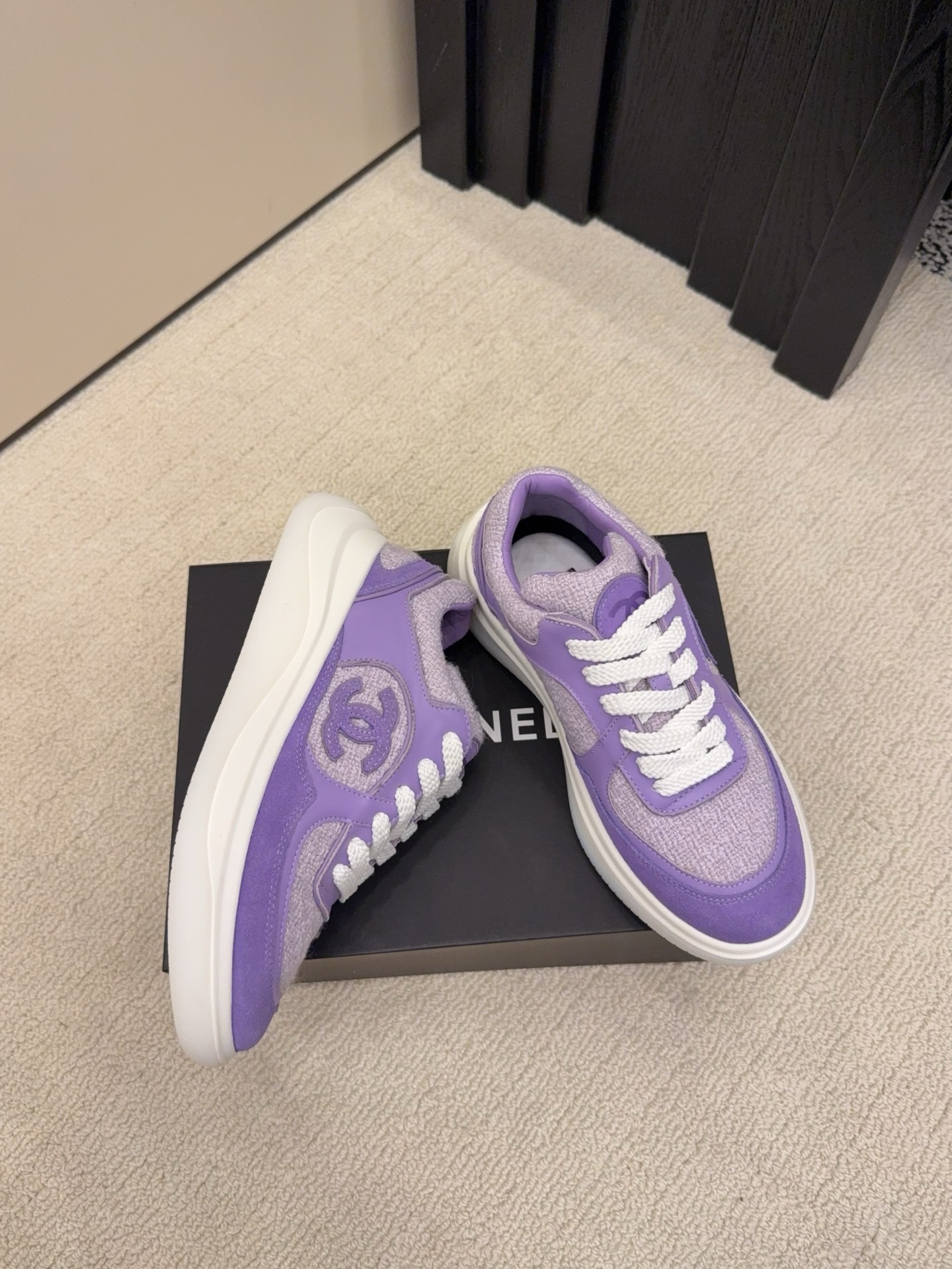 A pair of luxury Chanel purple tweed and suede sneakers with white chunky soles and white laces placed on a black designer shoe box. - Hình 4