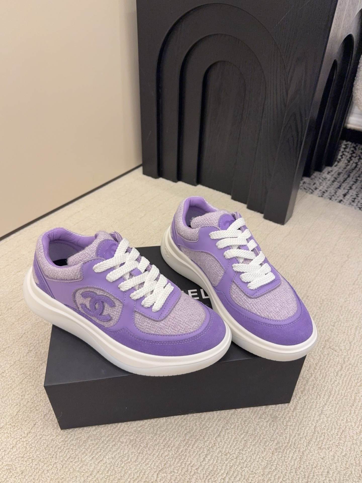 A pair of luxury Chanel purple tweed and suede sneakers with white chunky soles and white laces placed on a black designer shoe box. - Hình 3