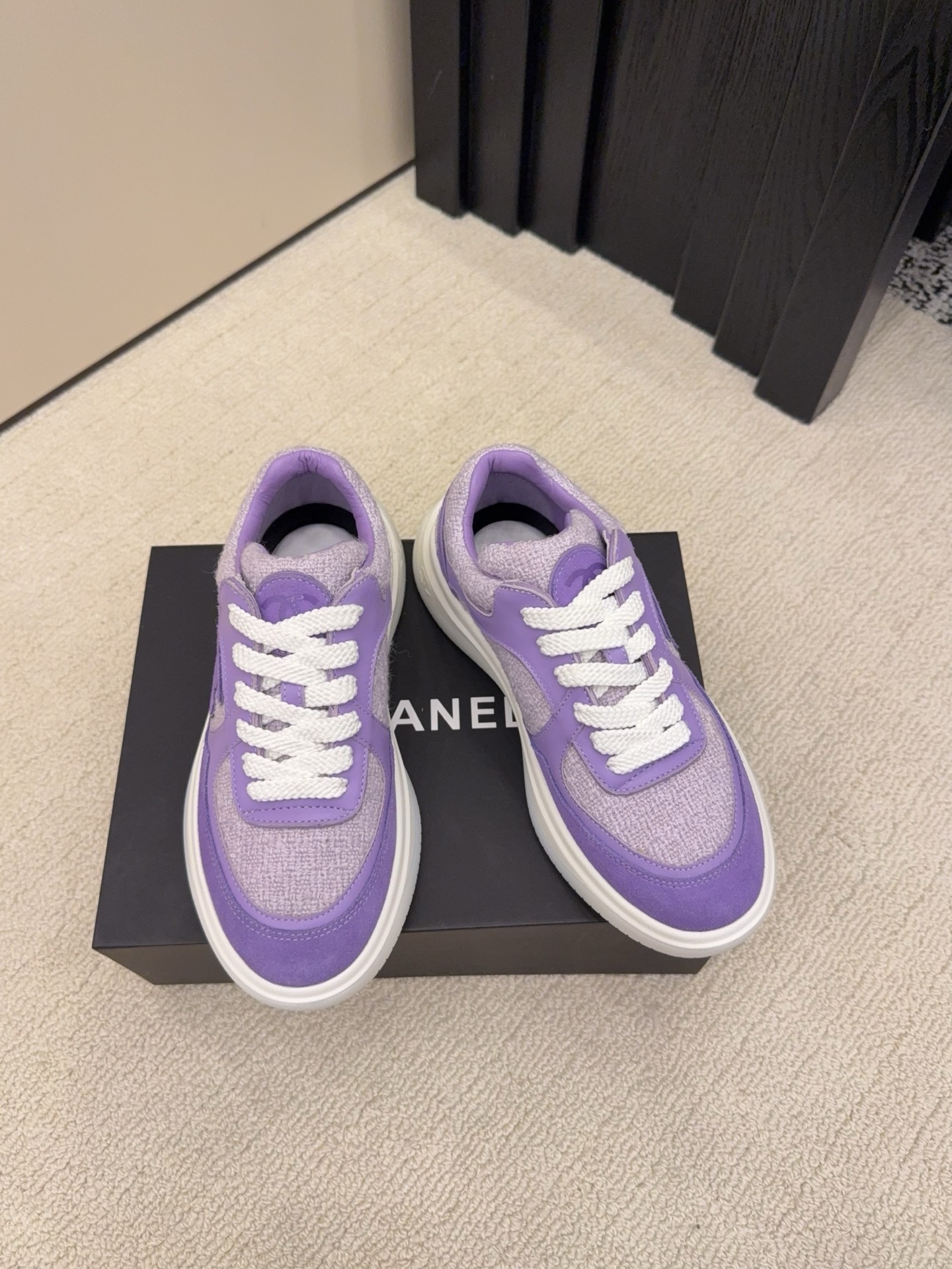 A pair of luxury Chanel purple tweed and suede sneakers with white chunky soles and white laces placed on a black designer shoe box. - Hình 2