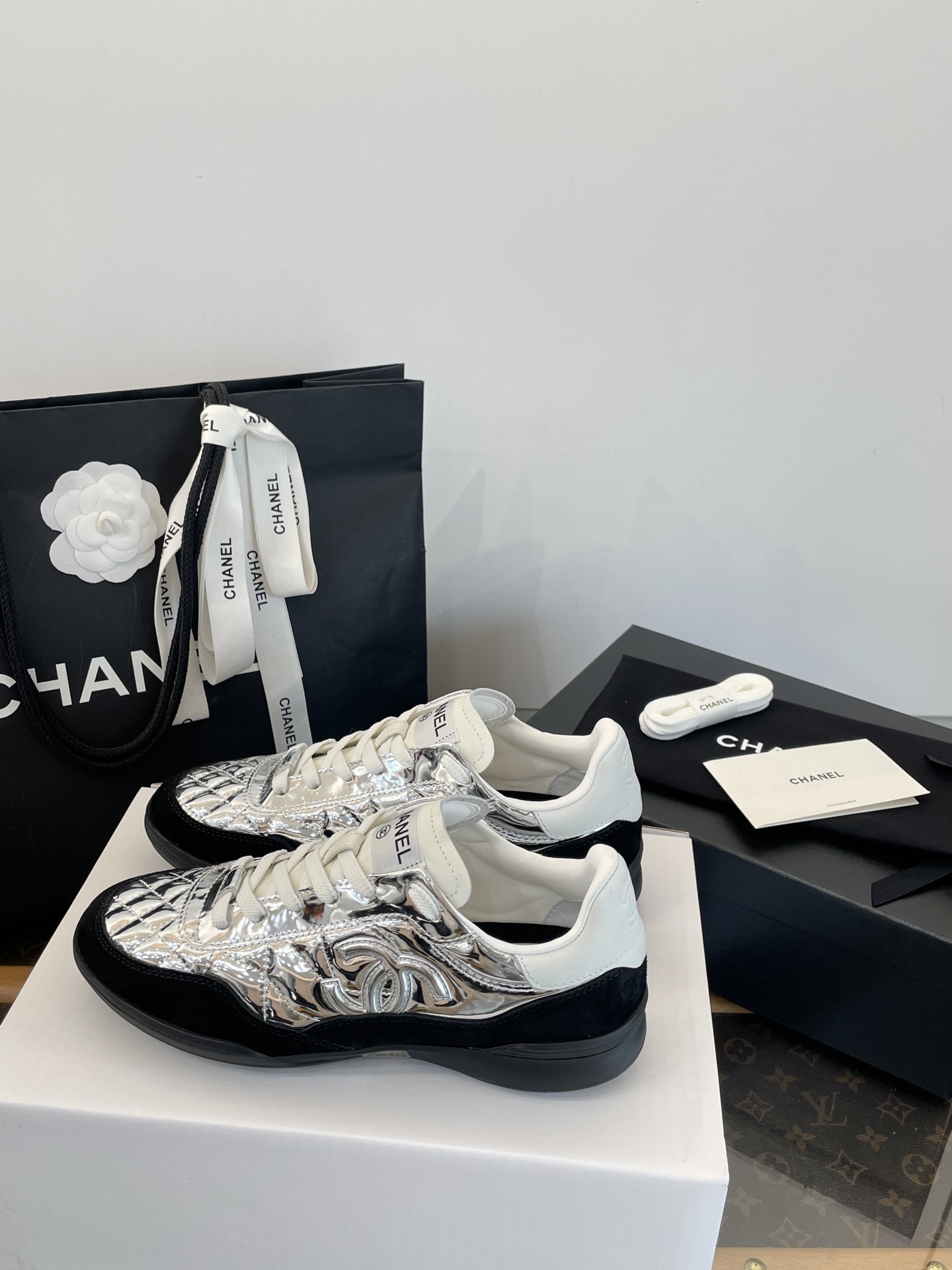 A pair of Chanel metallic silver quilted sneakers with black suede accents, shown with original black Chanel shopping bag, box, and dust bag. - Hình 9