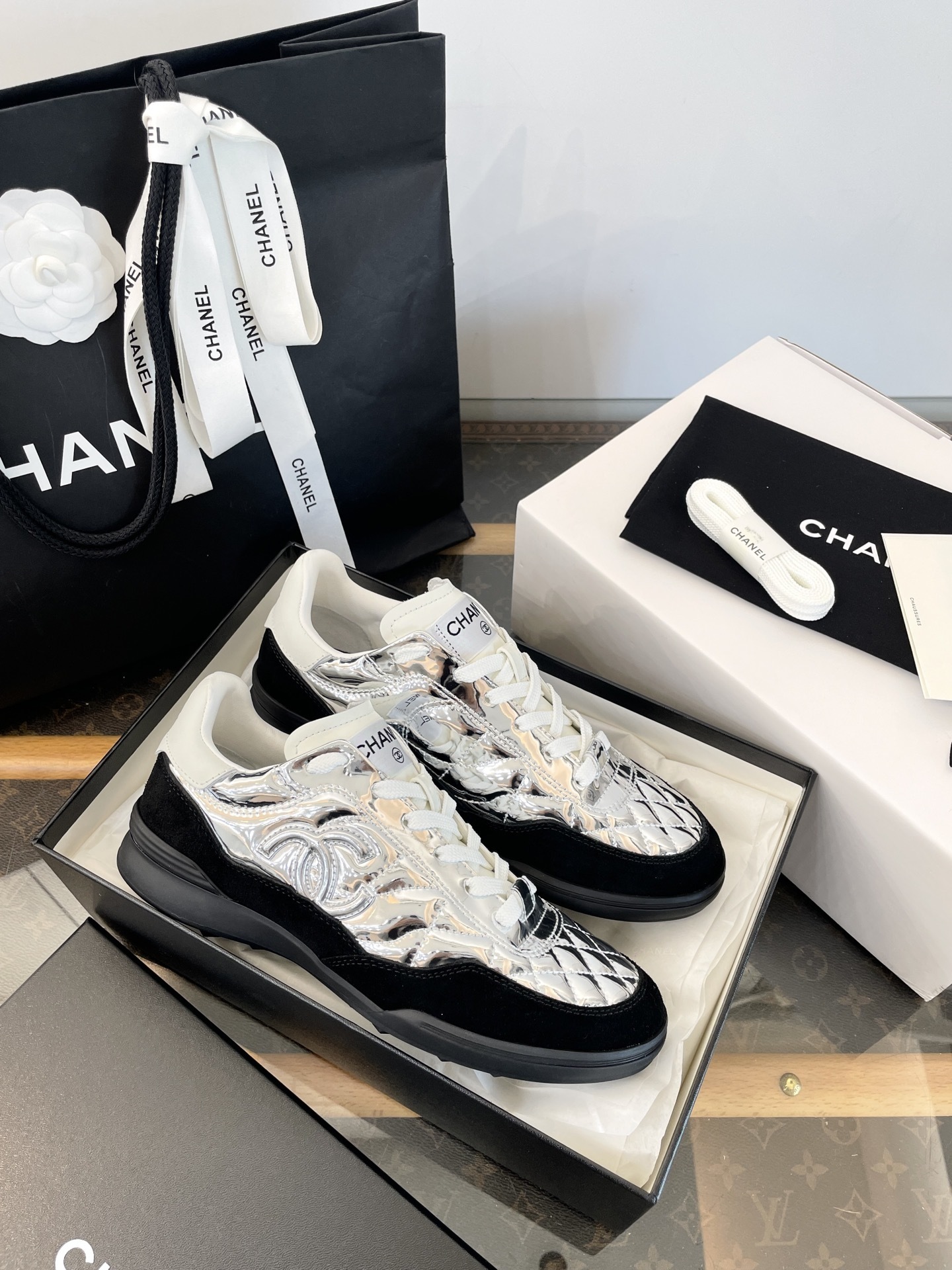 A pair of Chanel metallic silver quilted sneakers with black suede accents, shown with original black Chanel shopping bag, box, and dust bag. - Hình 8