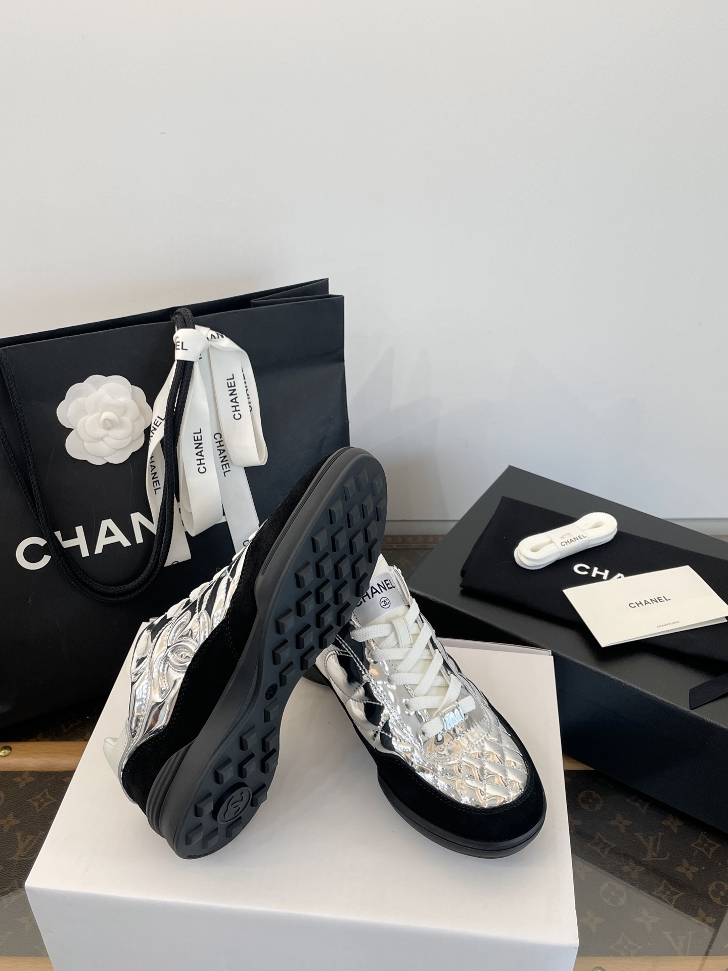 A pair of Chanel metallic silver quilted sneakers with black suede accents, shown with original black Chanel shopping bag, box, and dust bag. - Hình 7