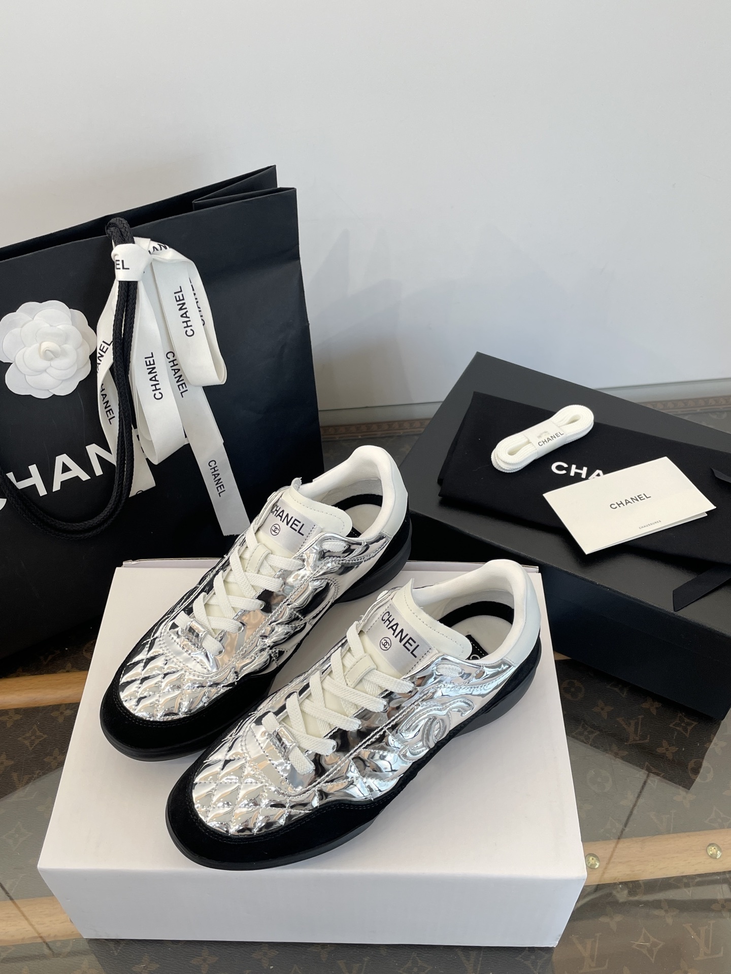 A pair of Chanel metallic silver quilted sneakers with black suede accents, shown with original black Chanel shopping bag, box, and dust bag. - Hình 6