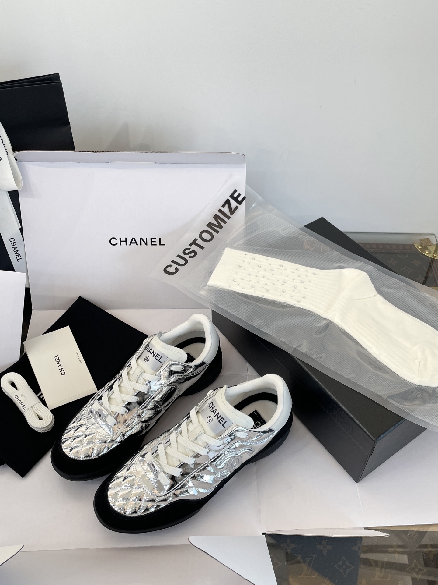 A pair of Chanel metallic silver quilted sneakers with black suede accents, shown with original black Chanel shopping bag, box, and dust bag. - Hình 5
