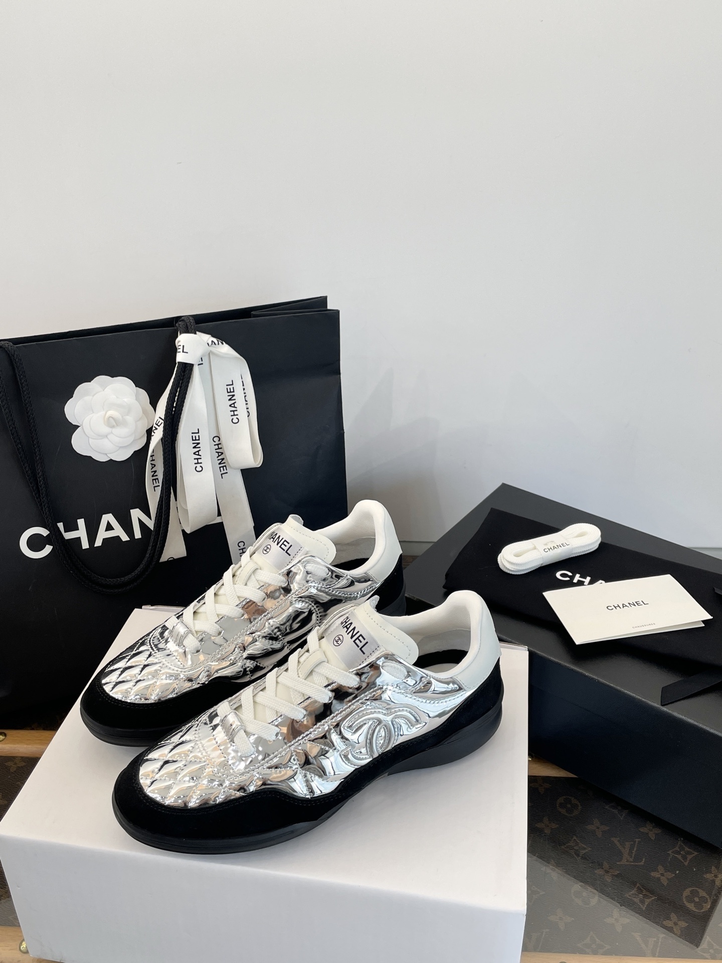A pair of Chanel metallic silver quilted sneakers with black suede accents, shown with original black Chanel shopping bag, box, and dust bag. - Hình 3