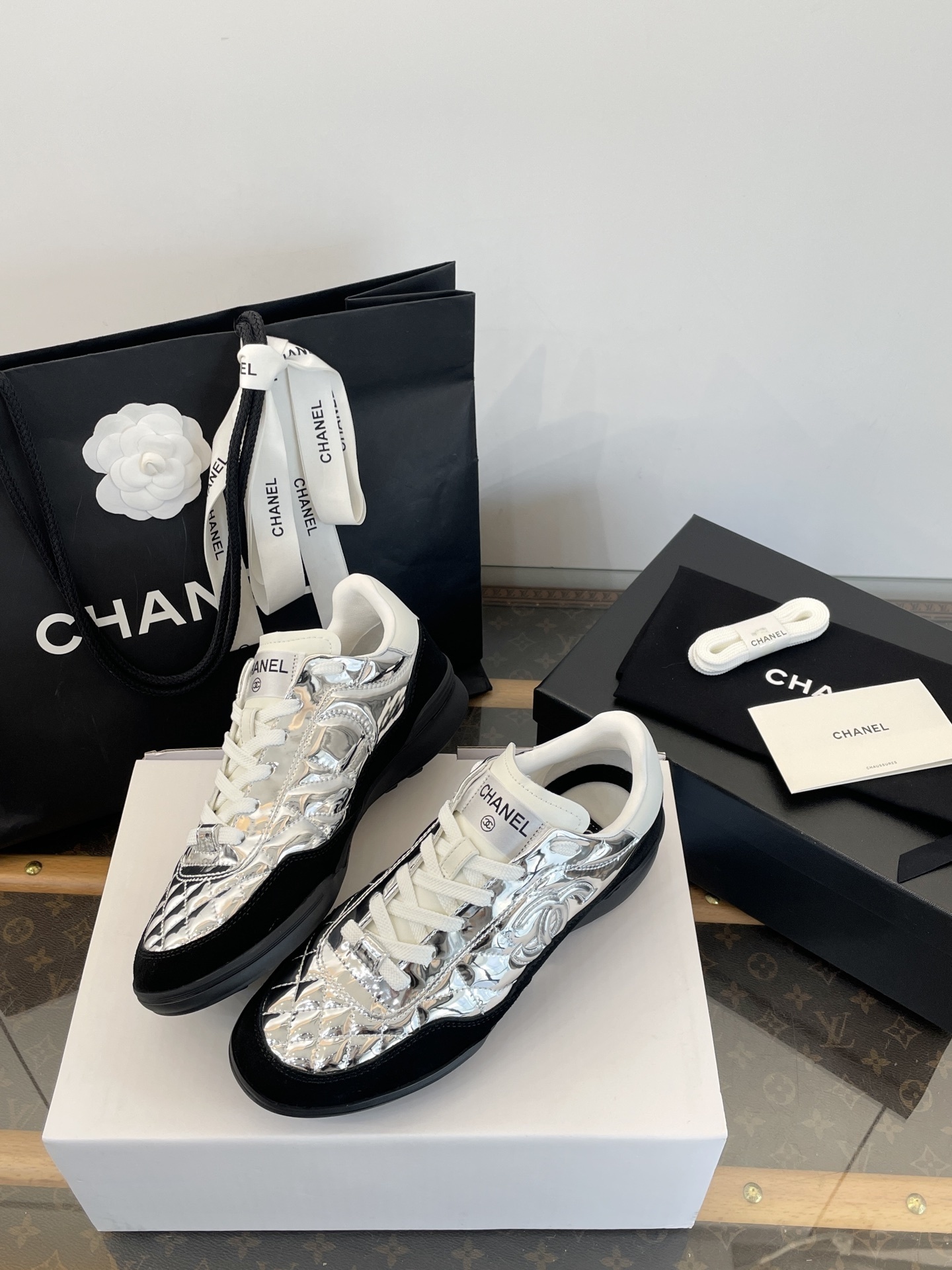 A pair of Chanel metallic silver quilted sneakers with black suede accents, shown with original black Chanel shopping bag, box, and dust bag. - Hình 2