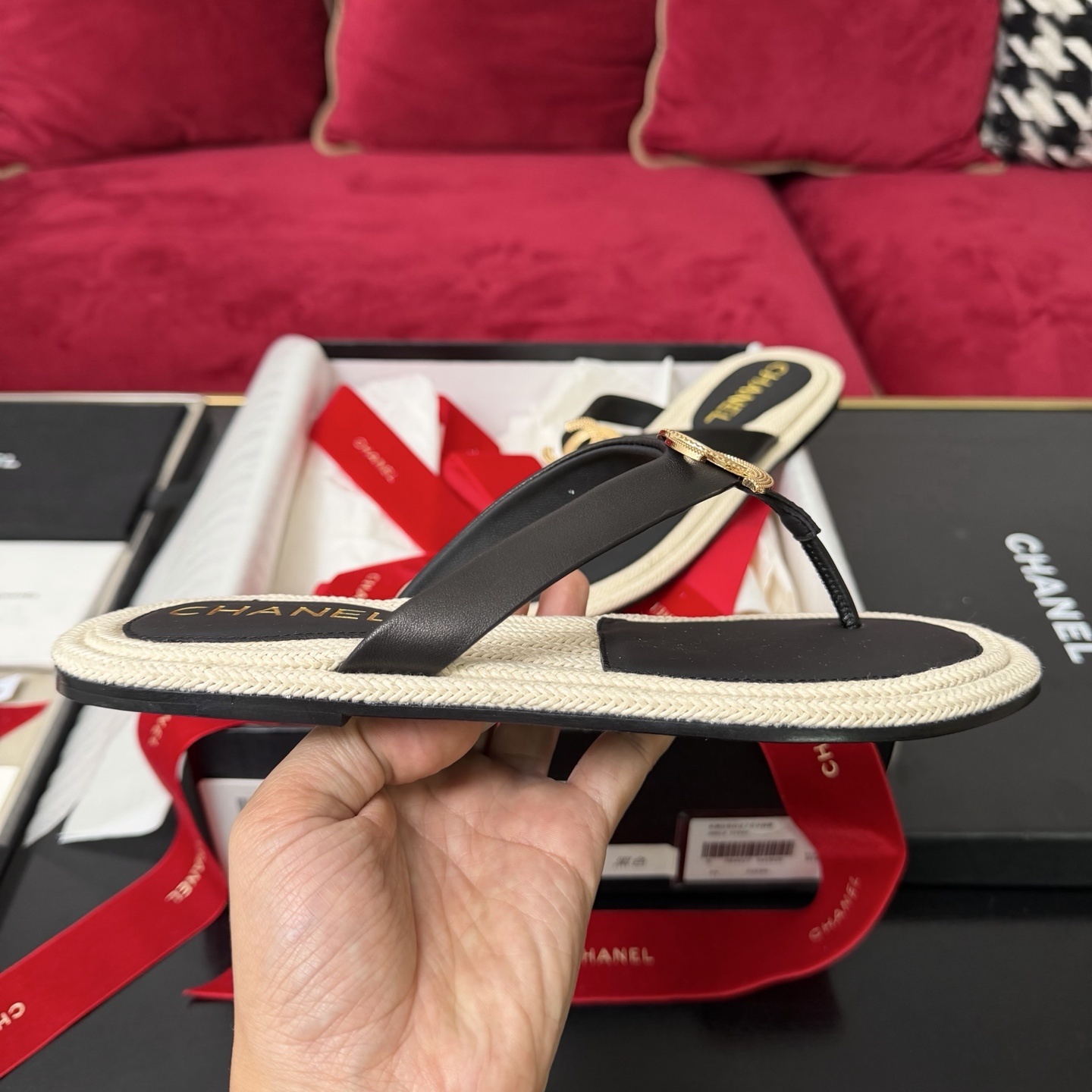 Close-up of Chanel black leather thong sandals with gold CC logo hardware and beige woven soles in a luxury box. - Hình 5