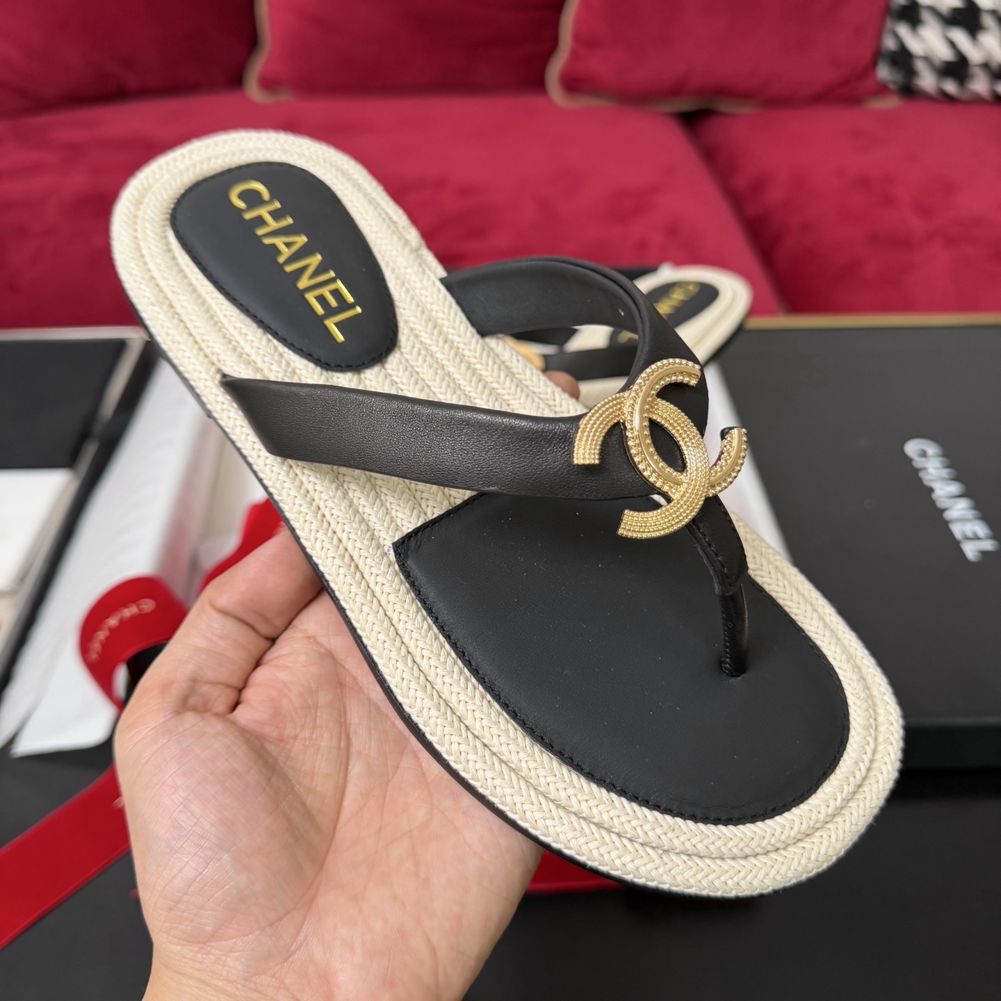 Close-up of Chanel black leather thong sandals with gold CC logo hardware and beige woven soles in a luxury box. - Hình 4