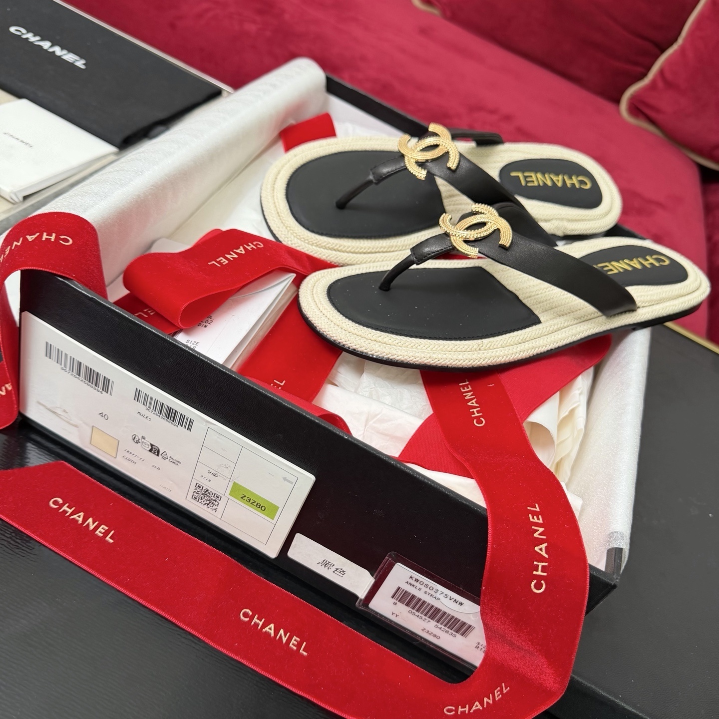 Close-up of Chanel black leather thong sandals with gold CC logo hardware and beige woven soles in a luxury box. - Hình 2