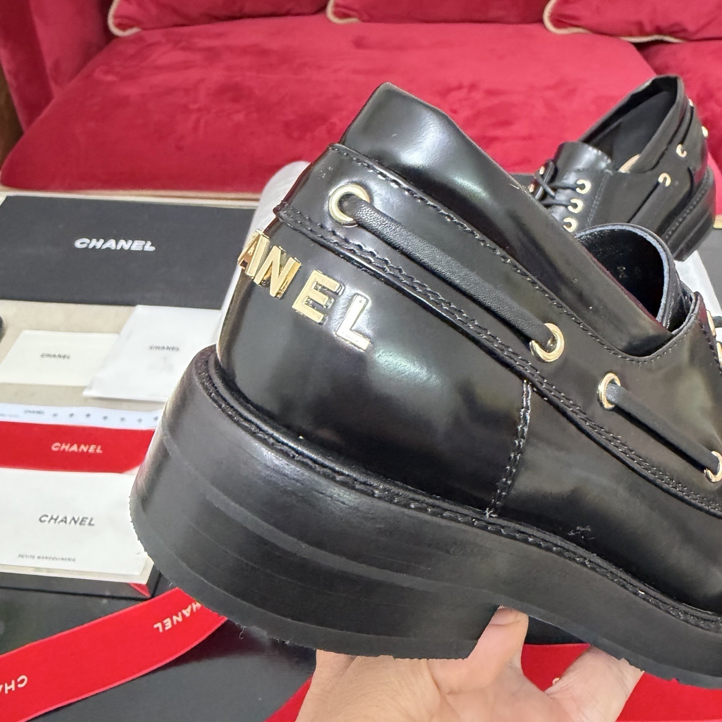 A pair of Chanel black leather lace-up loafers with gold CC logo hardware, displayed in a box with red velvet ribbons. - Hình 7