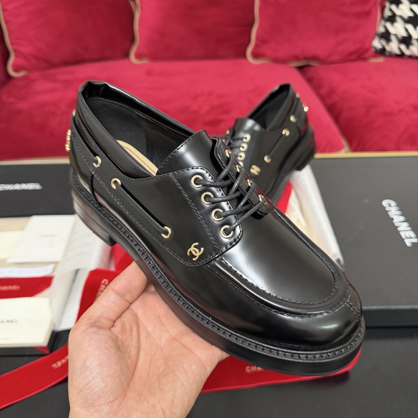 A pair of Chanel black leather lace-up loafers with gold CC logo hardware, displayed in a box with red velvet ribbons. - Hình 4